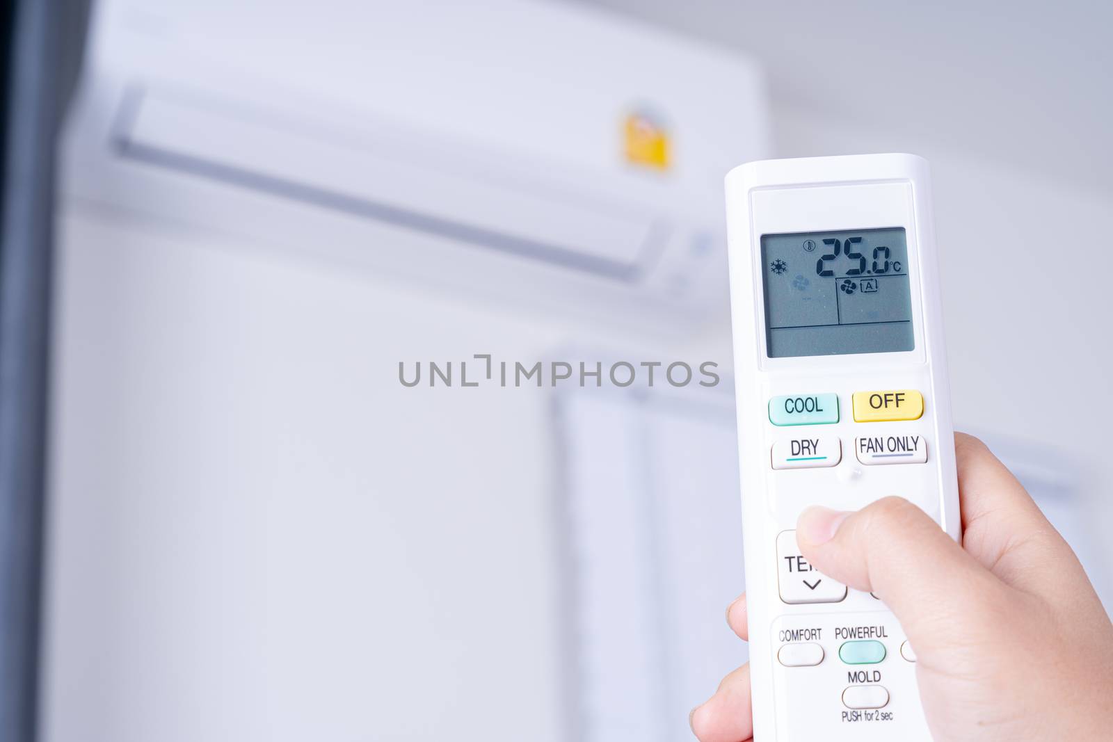 Human hand is using white remote of air conditioner for turn on or adjust temperature of air conditioner inside the room.