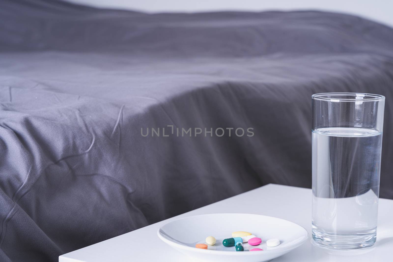 Close up pill drugs in the dish and a glass of water on nightstand in the bedroom. Healthcare and medical pharmacy concept