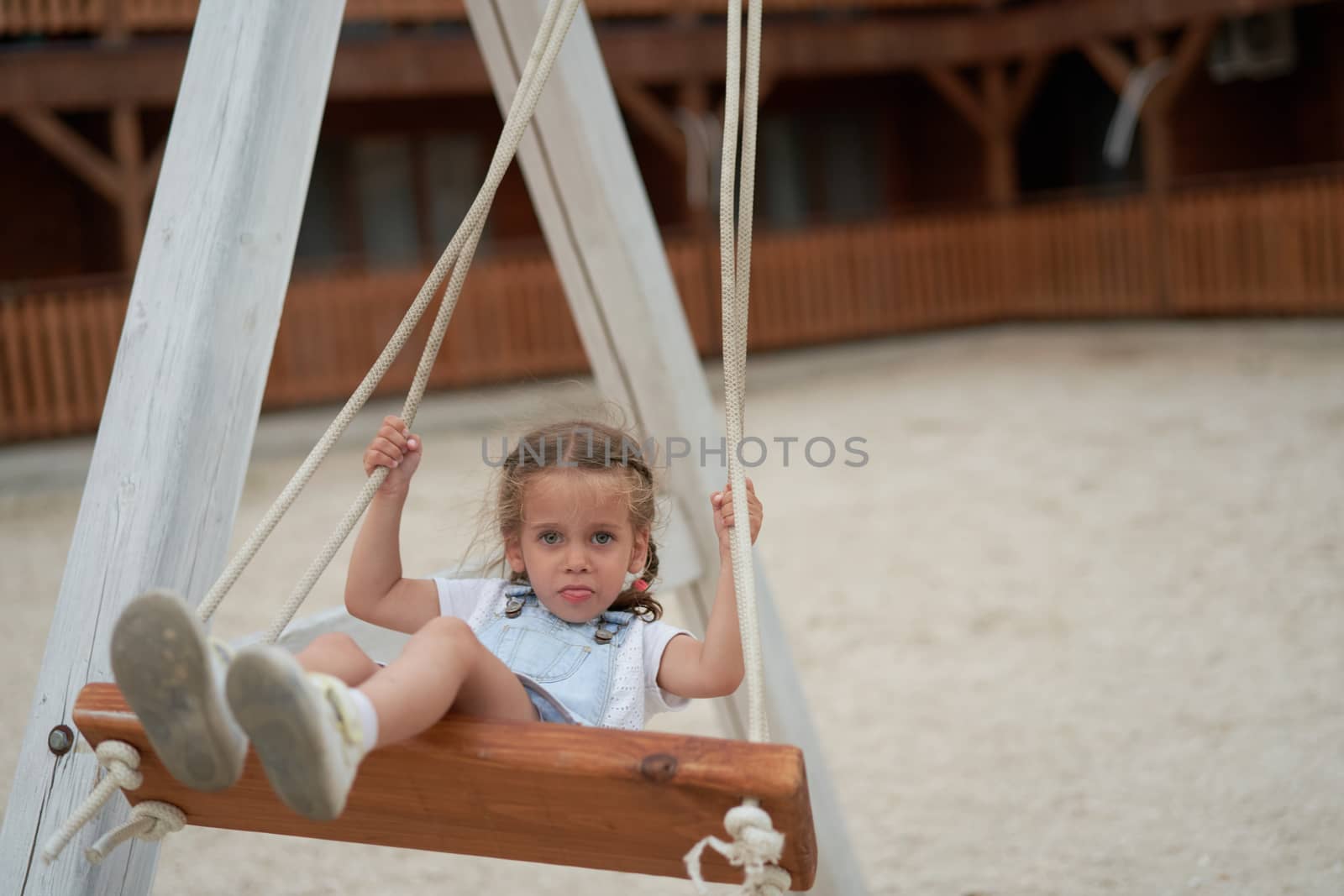 Playful kid swinging swing. Joyful little girl play having fun playground summertime by andreonegin