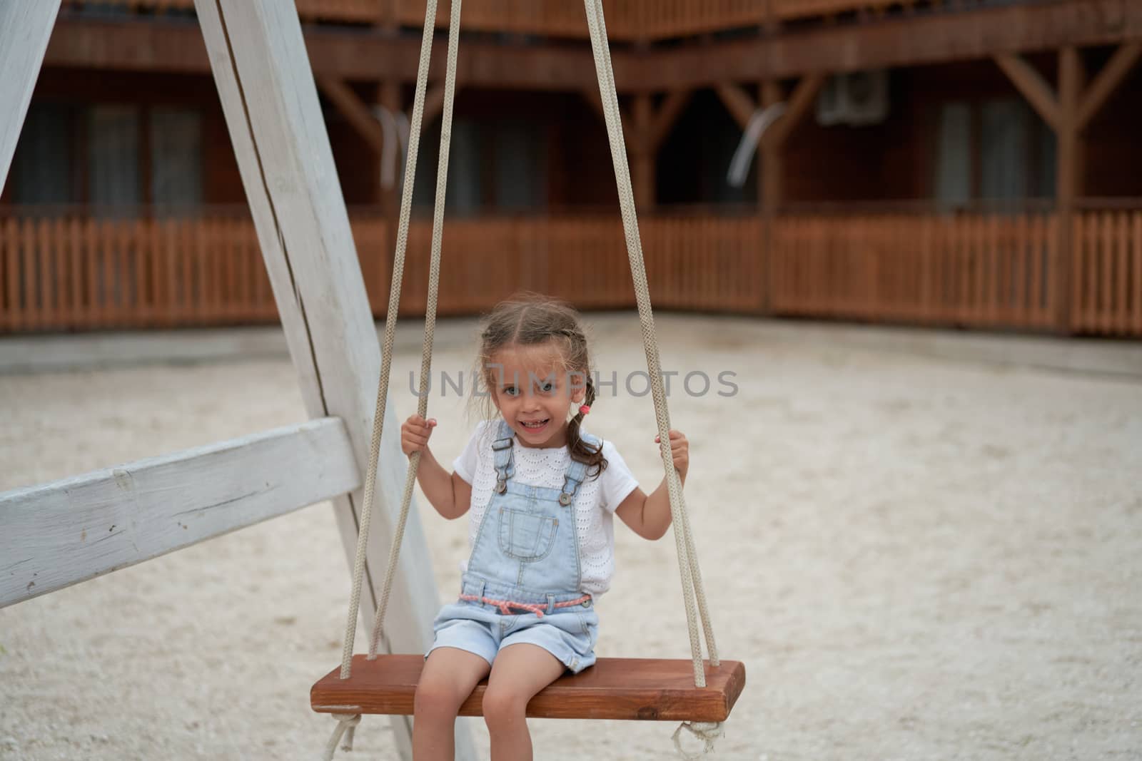 Playful kid swinging swing. Joyful little girl play having fun playground summertime by andreonegin