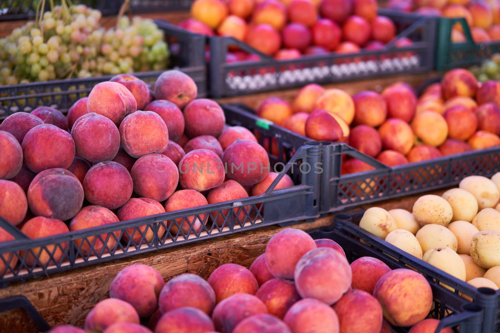 Fruit bazaar peaches grapes apricots ripe juicy lie plastic box showcase. by andreonegin