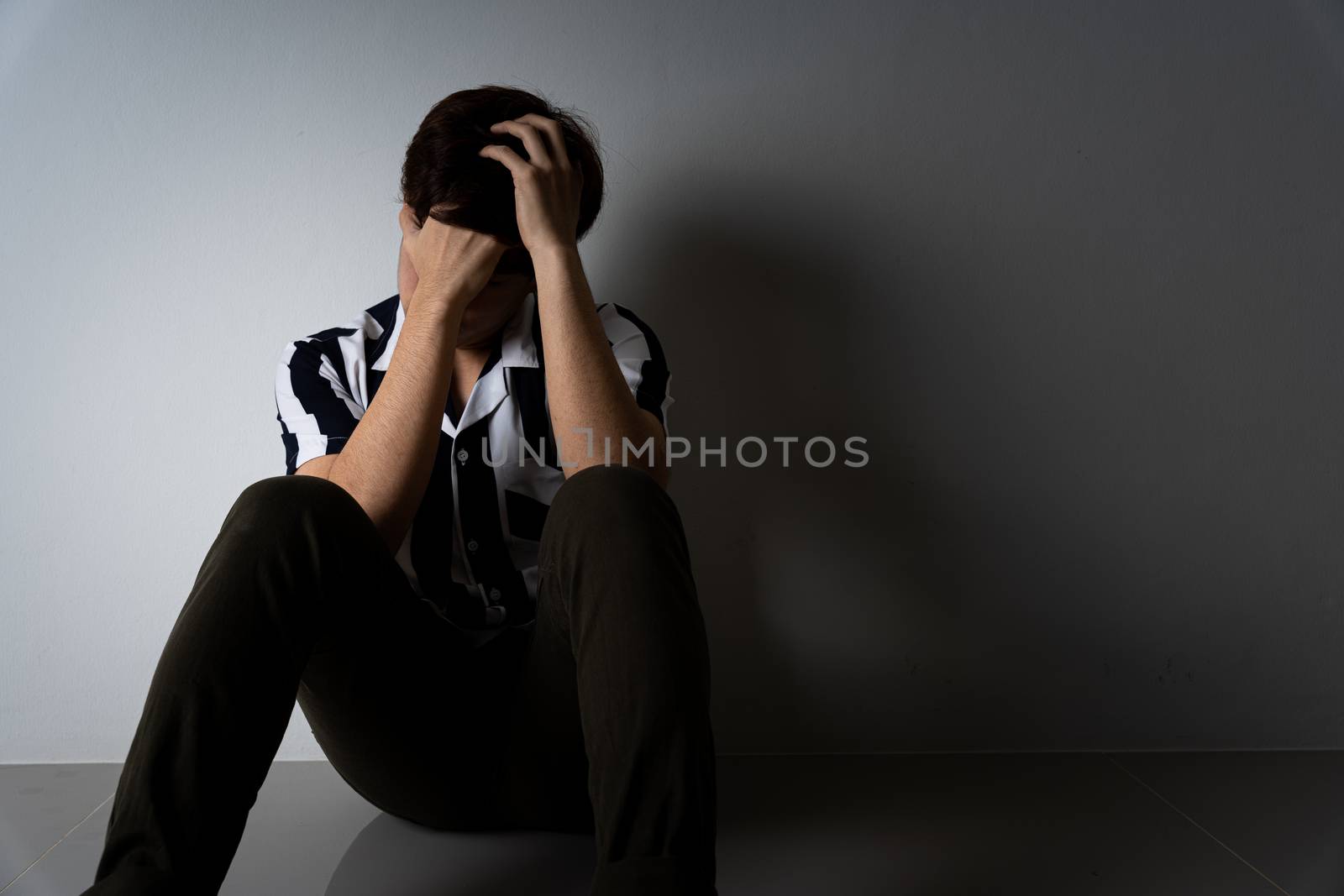 sad man hug her knee and cry sitting alone in a dark room. Depression, unhappy, stressed and anxiety disorder concept.