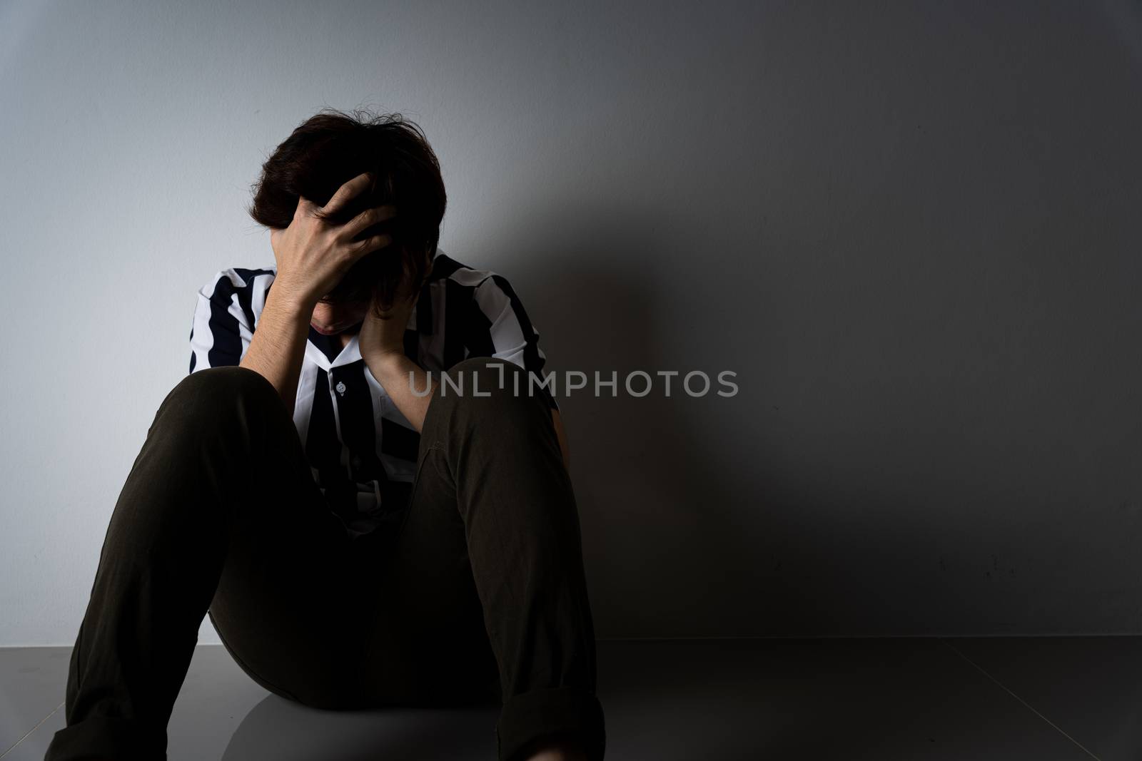 sad man hug her knee and cry sitting alone in a dark room. Depression, unhappy, stressed and anxiety disorder concept.