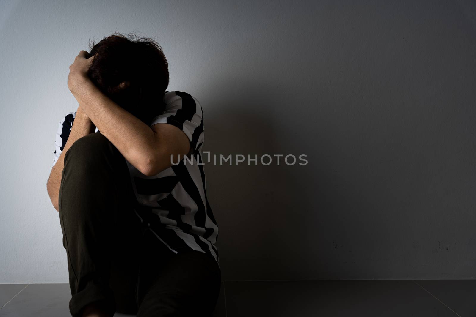 sad man hug her knee and cry sitting alone in a dark room. Depression, unhappy, stressed and anxiety disorder concept.