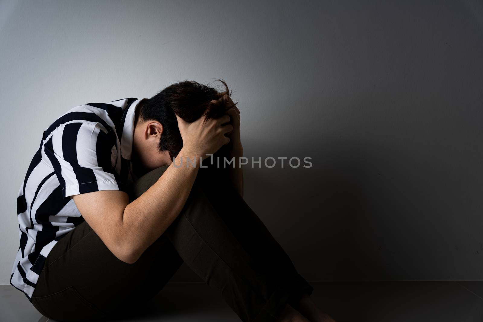 sad man hug her knee and cry sitting alone in a dark room. Depression, unhappy, stressed and anxiety disorder concept.