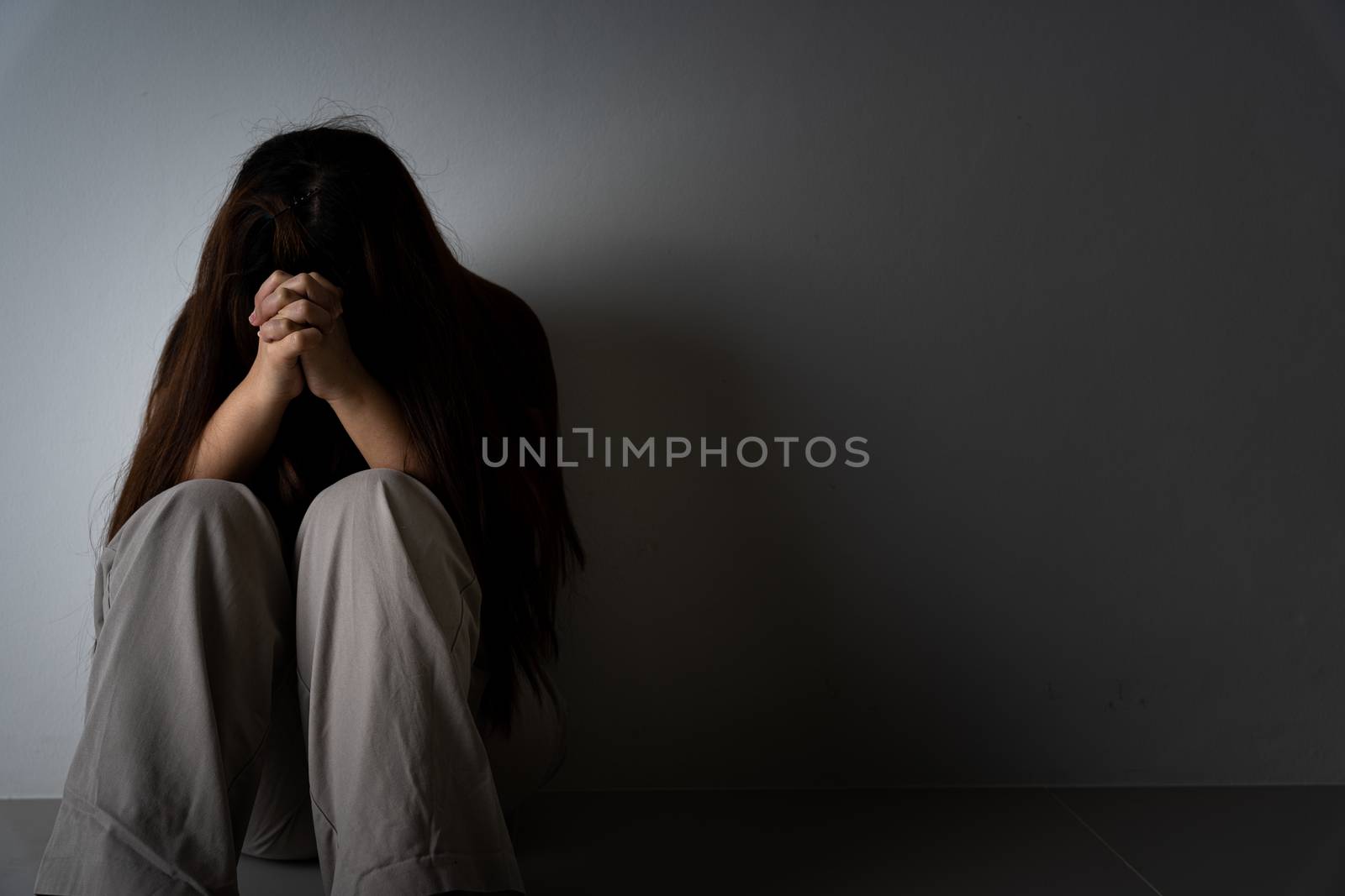 sad woman hug her knee and cry sitting alone in a dark room. Depression, unhappy, stressed and anxiety disorder concept.