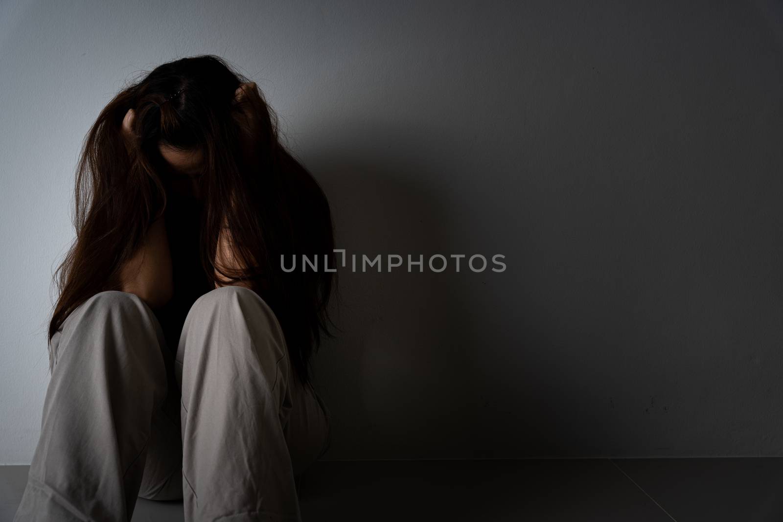 sad woman hug her knee and cry sitting alone in a dark room. Depression, unhappy, stressed and anxiety disorder concept.