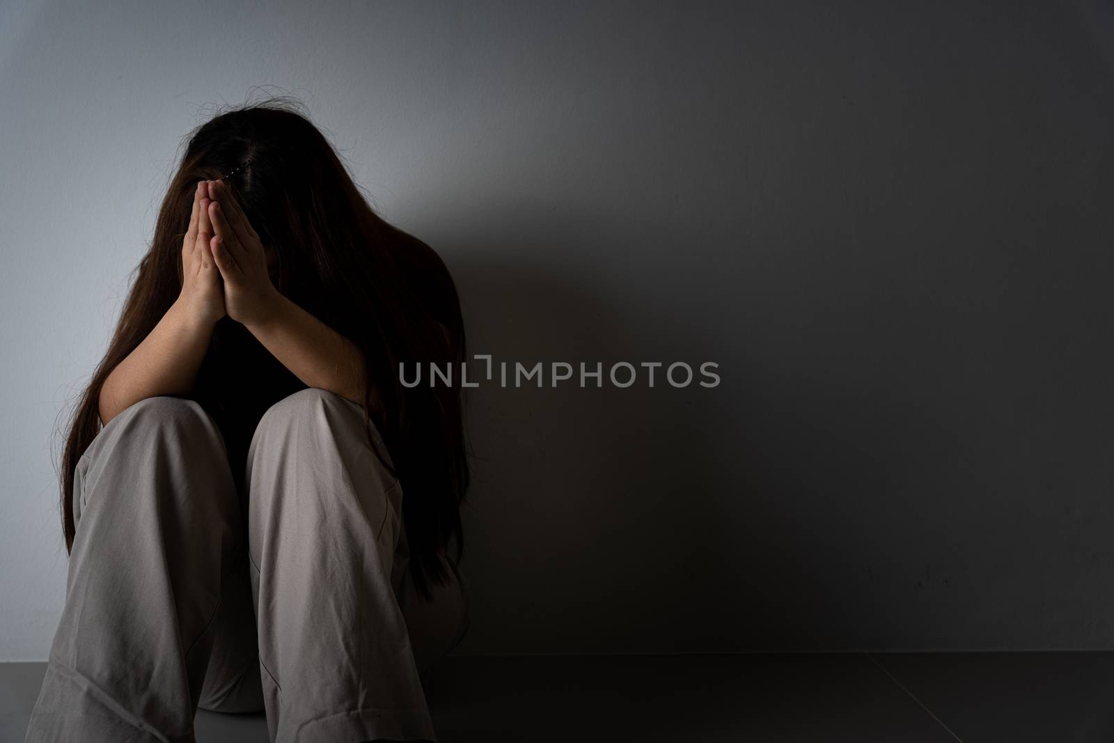 sad woman hug her knee and cry sitting alone in a dark room. Depression, unhappy, stressed and anxiety disorder concept.