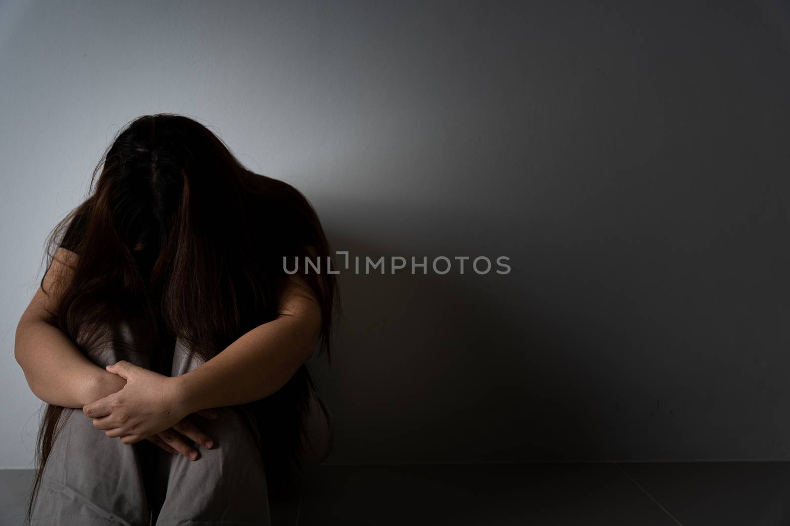 sad woman hug her knee and cry sitting alone in a dark room. Depression, unhappy, stressed and anxiety disorder concept.