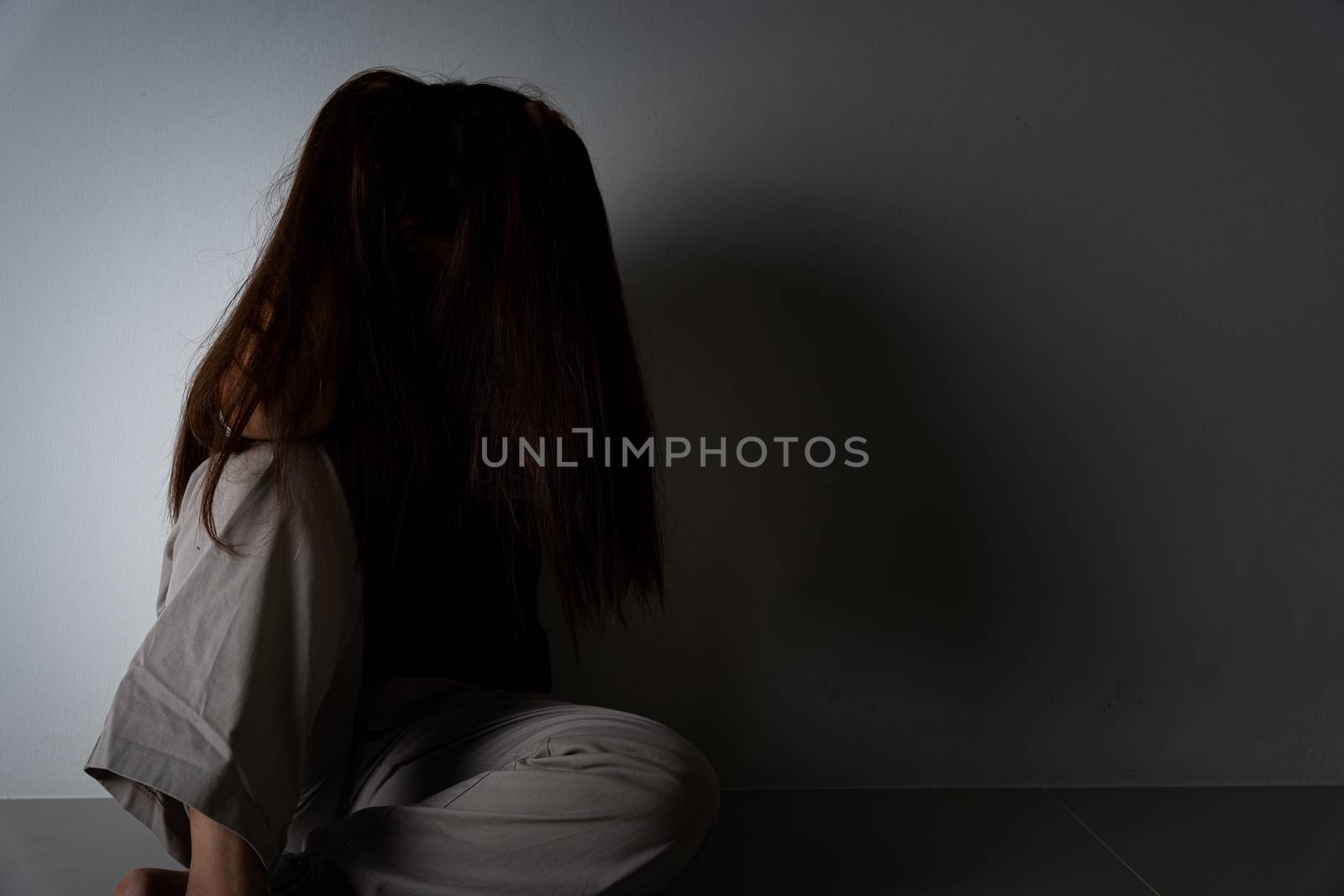 sad woman hug her knee and cry sitting alone in a dark room. Depression, unhappy, stressed and anxiety disorder concept.