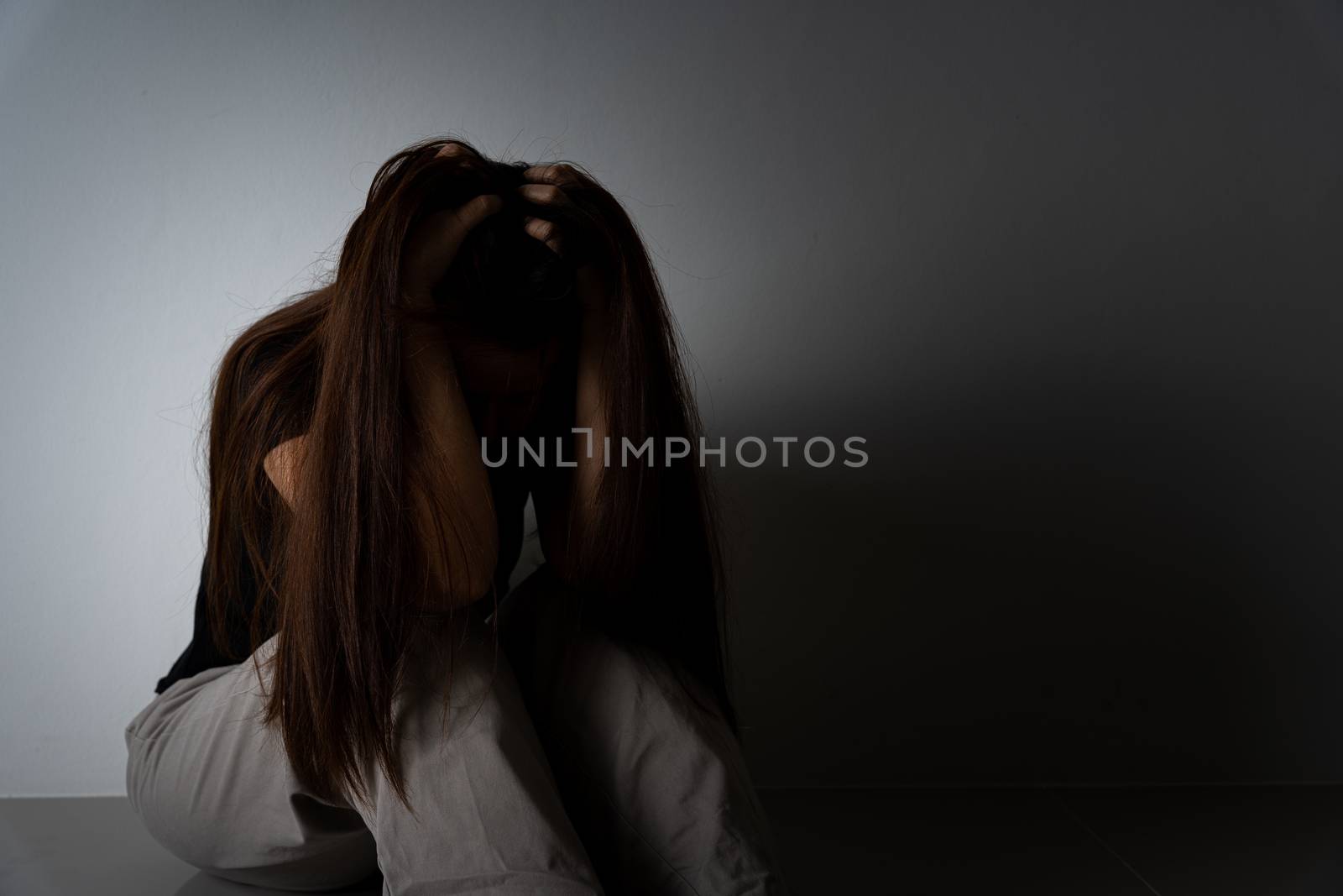 sad woman hug her knee and cry sitting alone in a dark room. Depression, unhappy, stressed and anxiety disorder concept.