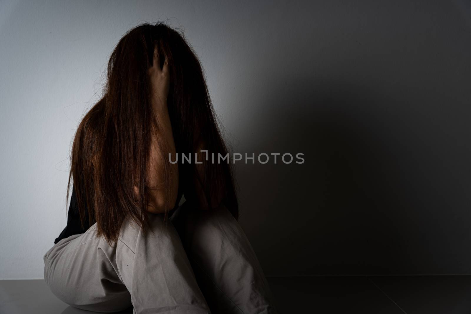sad woman hug her knee and cry sitting alone in a dark room. Depression, unhappy, stressed and anxiety disorder concept.