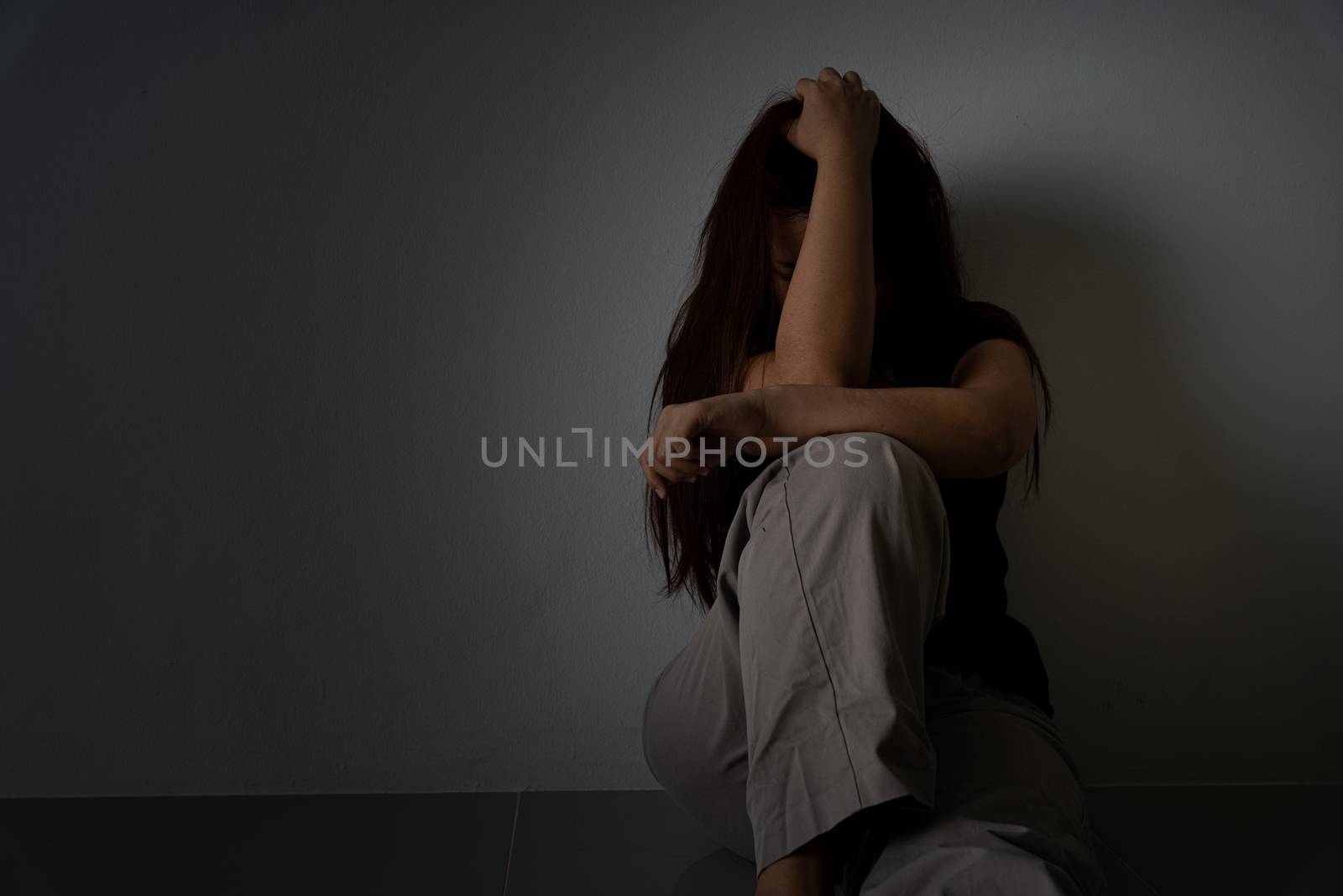 sad woman hug her knee and cry sitting alone in a dark room. Depression, unhappy, stressed and anxiety disorder concept.