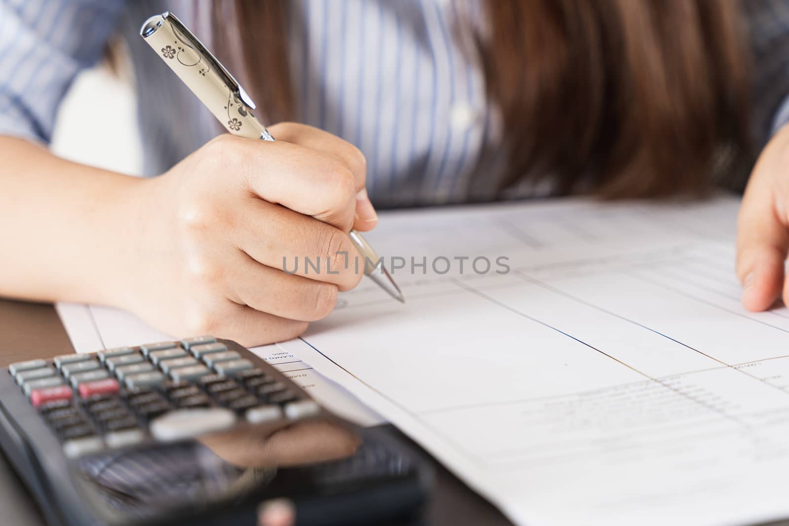 businesswoman working on desk office holding pen and using a calculator to calculate the numbers. Expenses, taxes, home budget finance accounting concept.