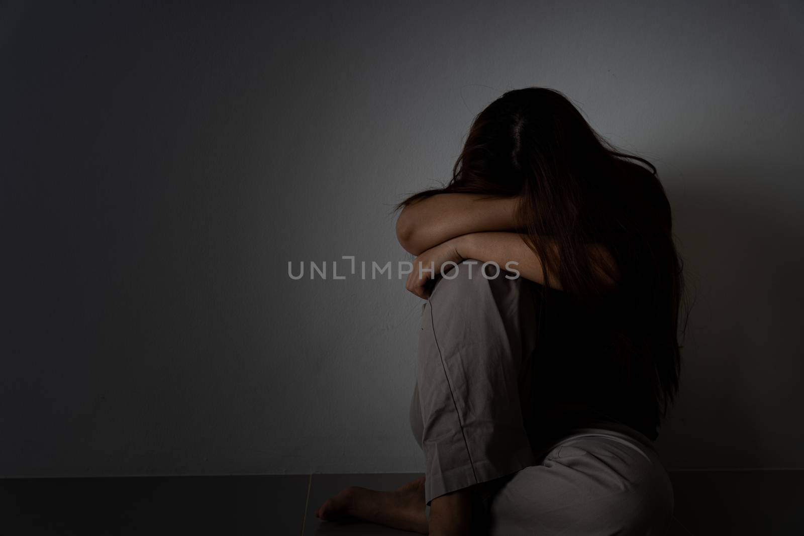 sad woman hug her knee and cry sitting alone in a dark room. Depression, unhappy, stressed and anxiety disorder concept.