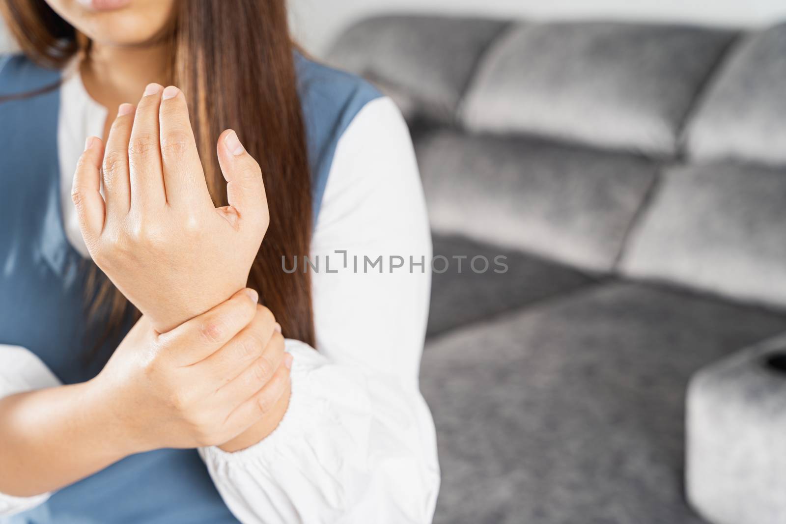 Young woman suffering from wrist pain while sitting on sofa at home. Healthcare medical or daily life concept.