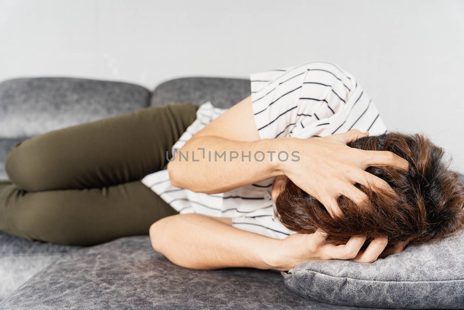 Young man suffering from head pain while lying on sofa at home. Healthcare medical or daily life concept.
