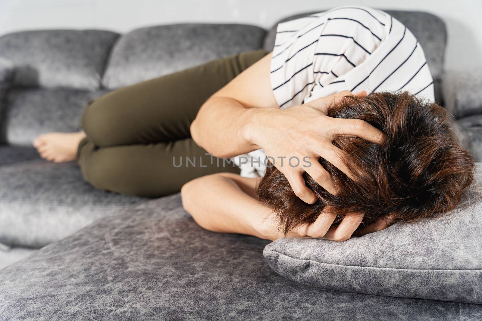 Young man suffering from head pain while lying on sofa at home. Healthcare medical or daily life concept. by mikesaran