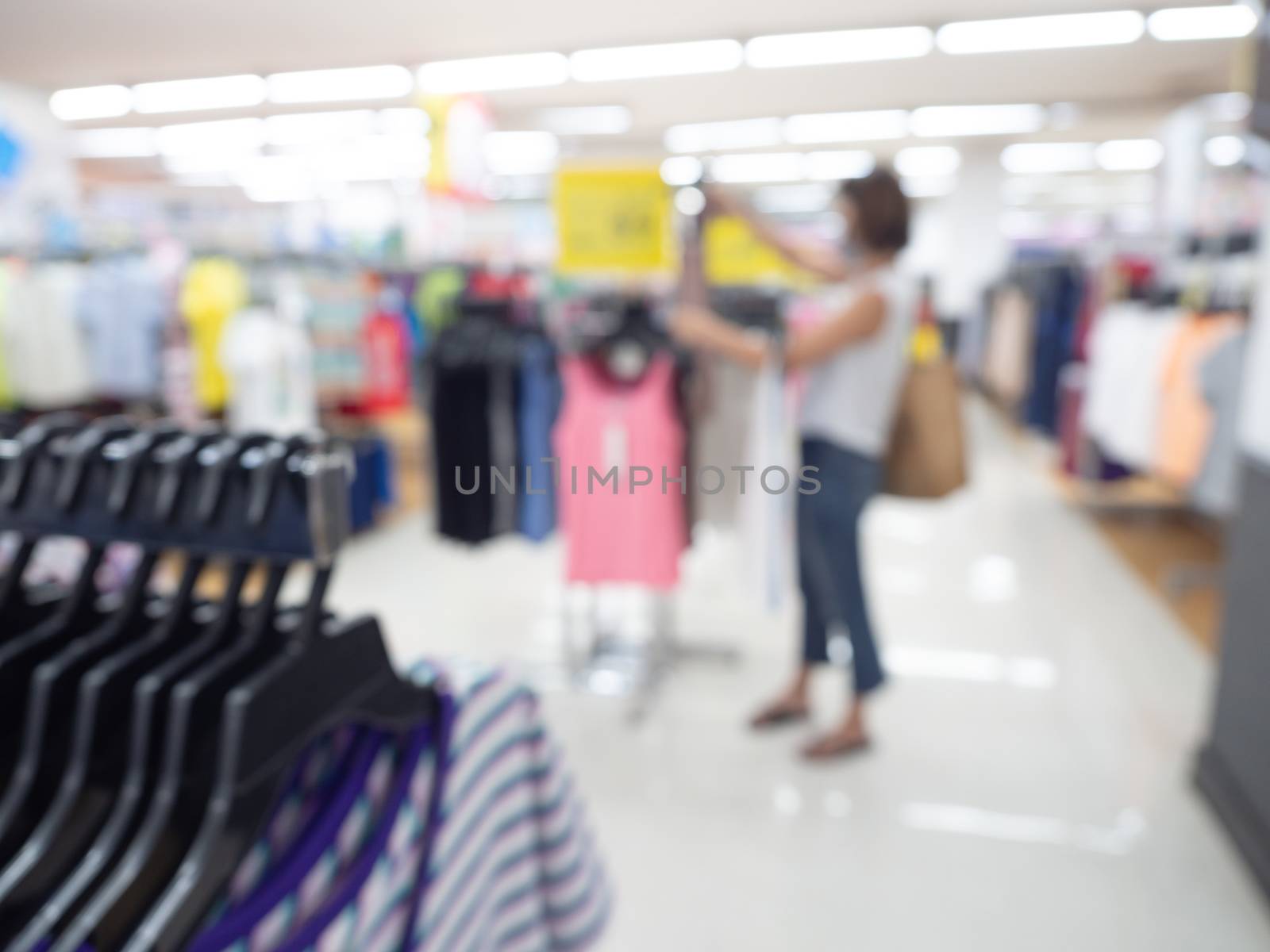 Supermarket blur background. Blurred shopping woman with hanging clothes in shopping mall.