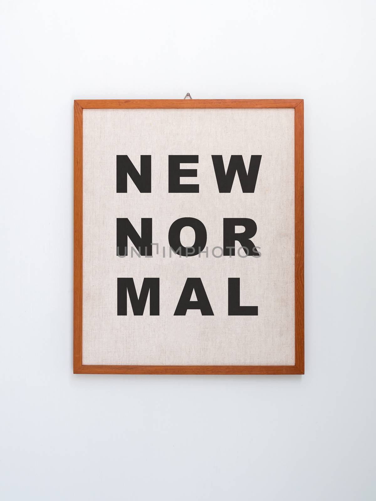 "New normal" word on light brown canvas on hanging wooden frame isolated on white background, vertical style.