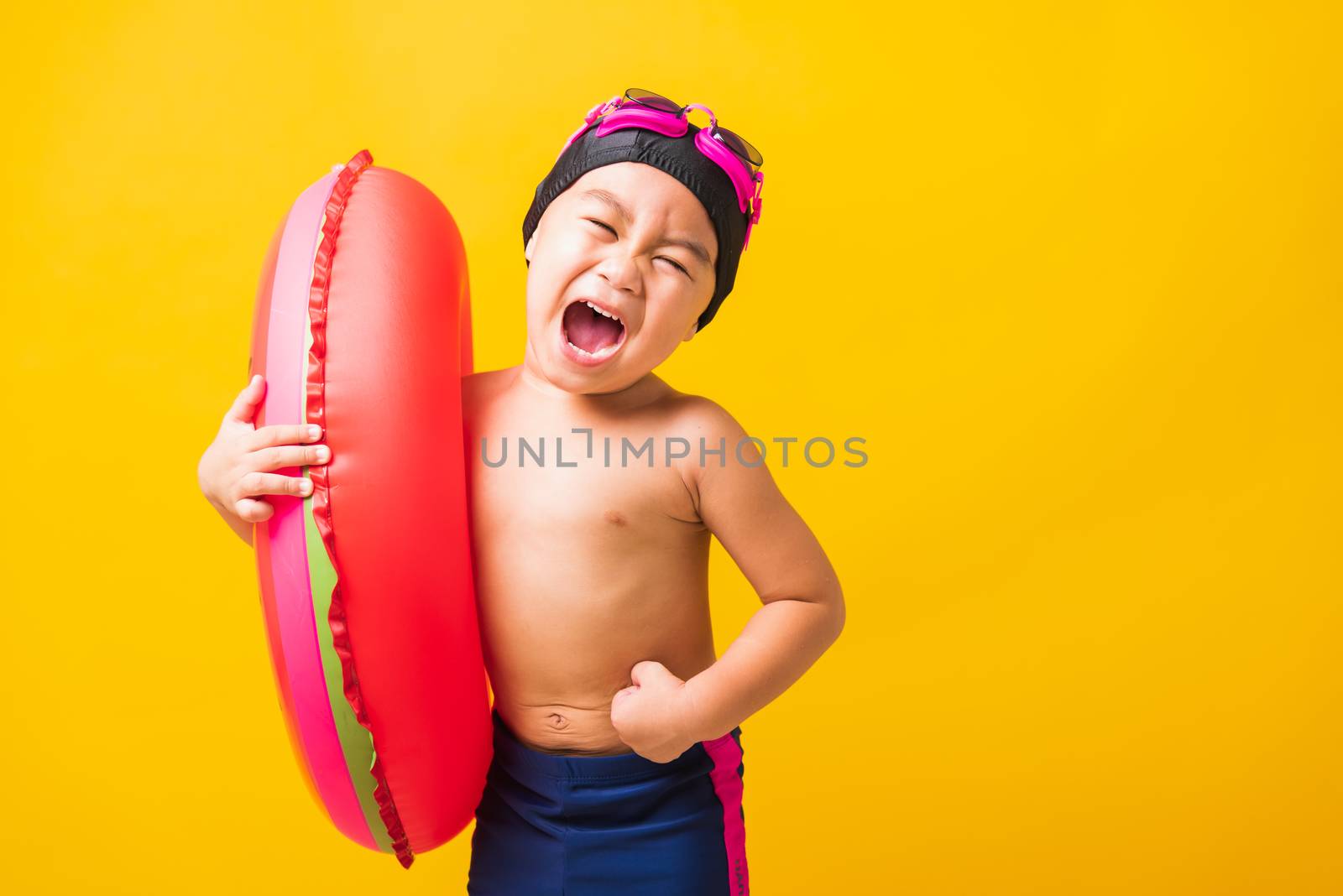 Summer vacation concept, Portrait Asian happy cute little child boy wear goggles and swimsuit hold watermelon inflatable ring, Kid having fun on summer vacation, studio shot isolated yellow background