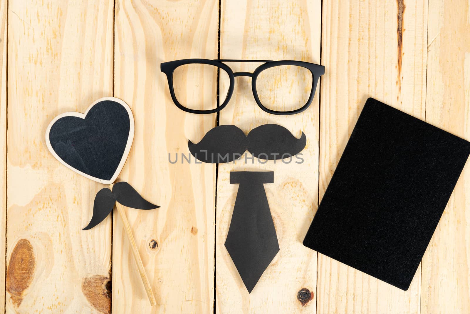 Happy Father Day background concept with glasses, blackboard, black heart shape, tie and black mustache on wooden background with copy space for text.
