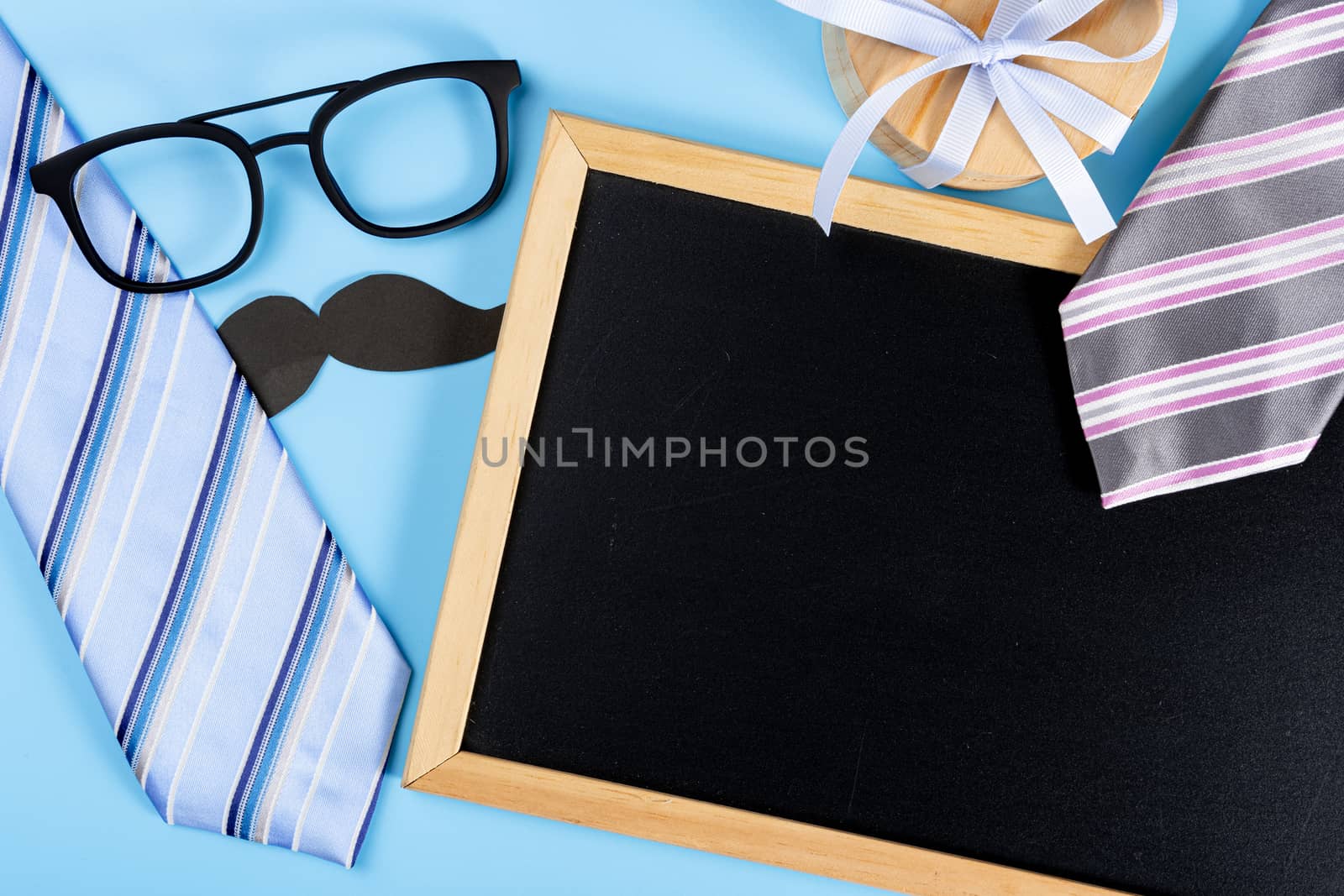 Happy Father Day background concept with blue and pink necktie, glasses, gift box, black mustache and blackboard on blue background with copy space for text.