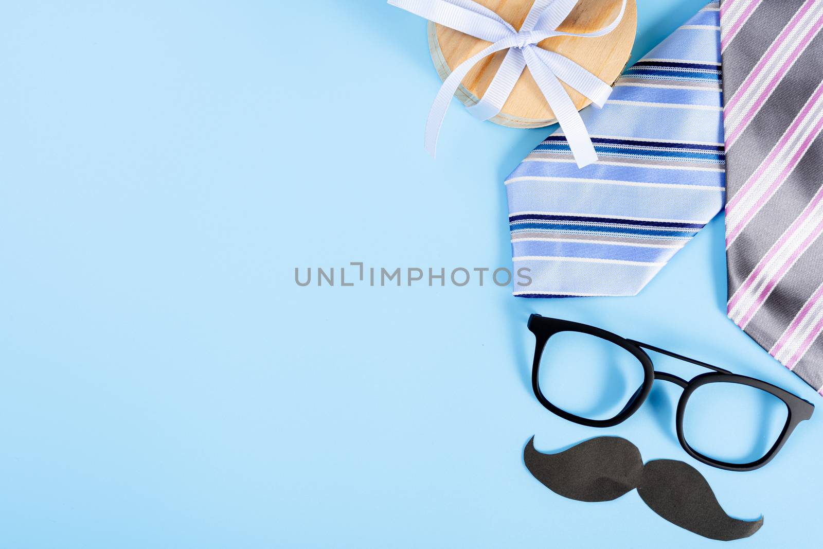Happy Father Day background concept with blue necktie, glasses, gift box and black mustache on blue background with copy space for text.