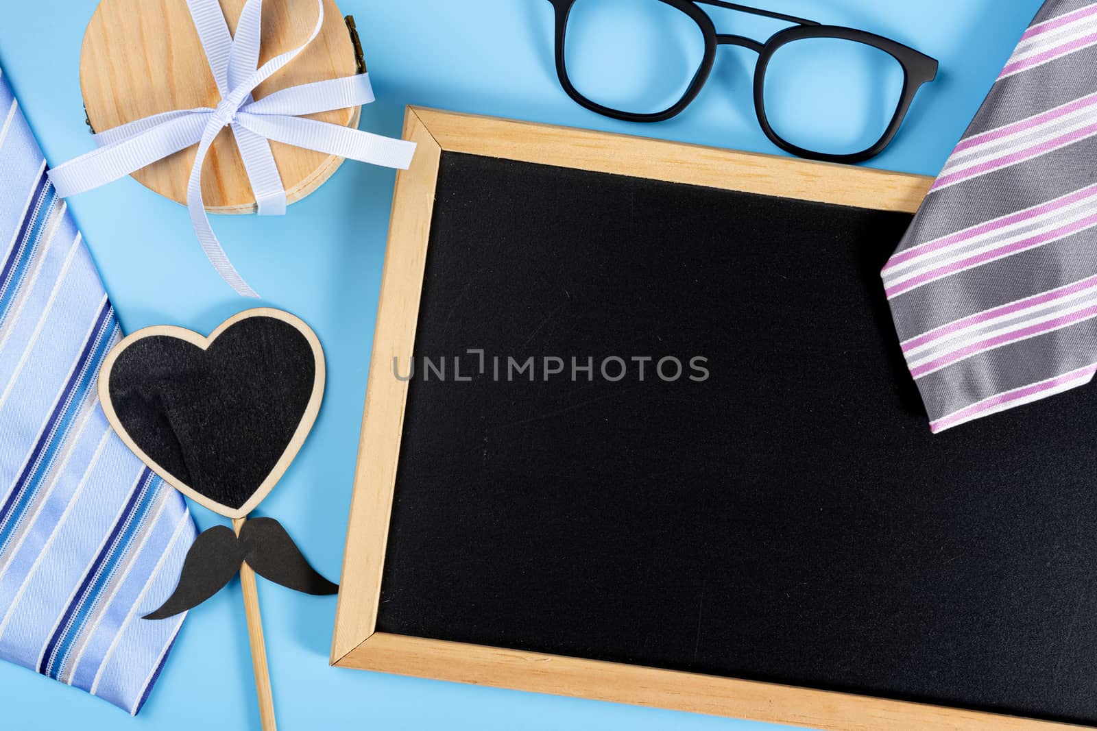 Happy Father Day background concept with blue and pink necktie, glasses, gift box, black heart shape and blackboard on blue background with copy space for text.