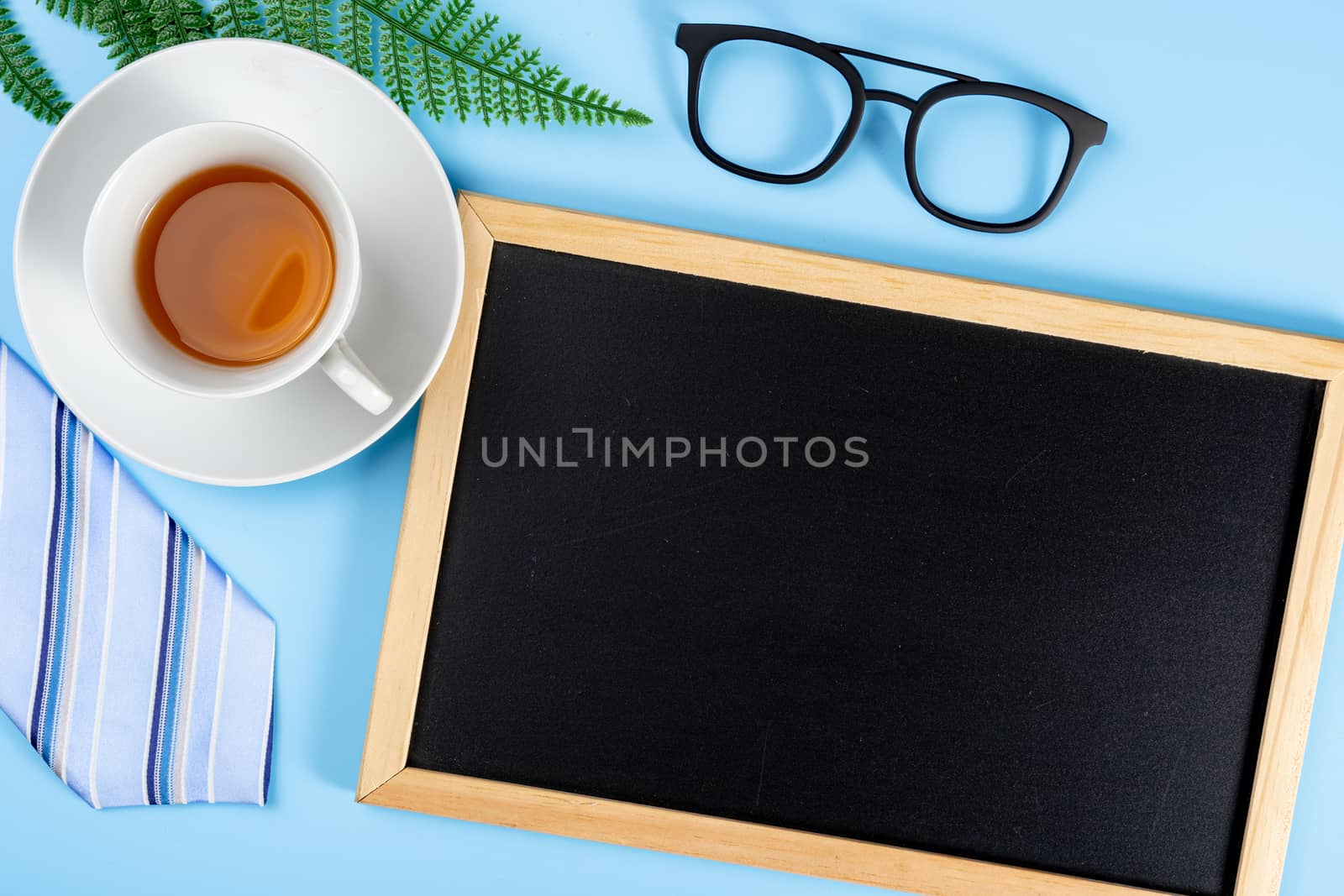 Happy Father Day background concept with blue necktie glasses, leaf, cup of tea and blackboard on blue background with copy space for text.