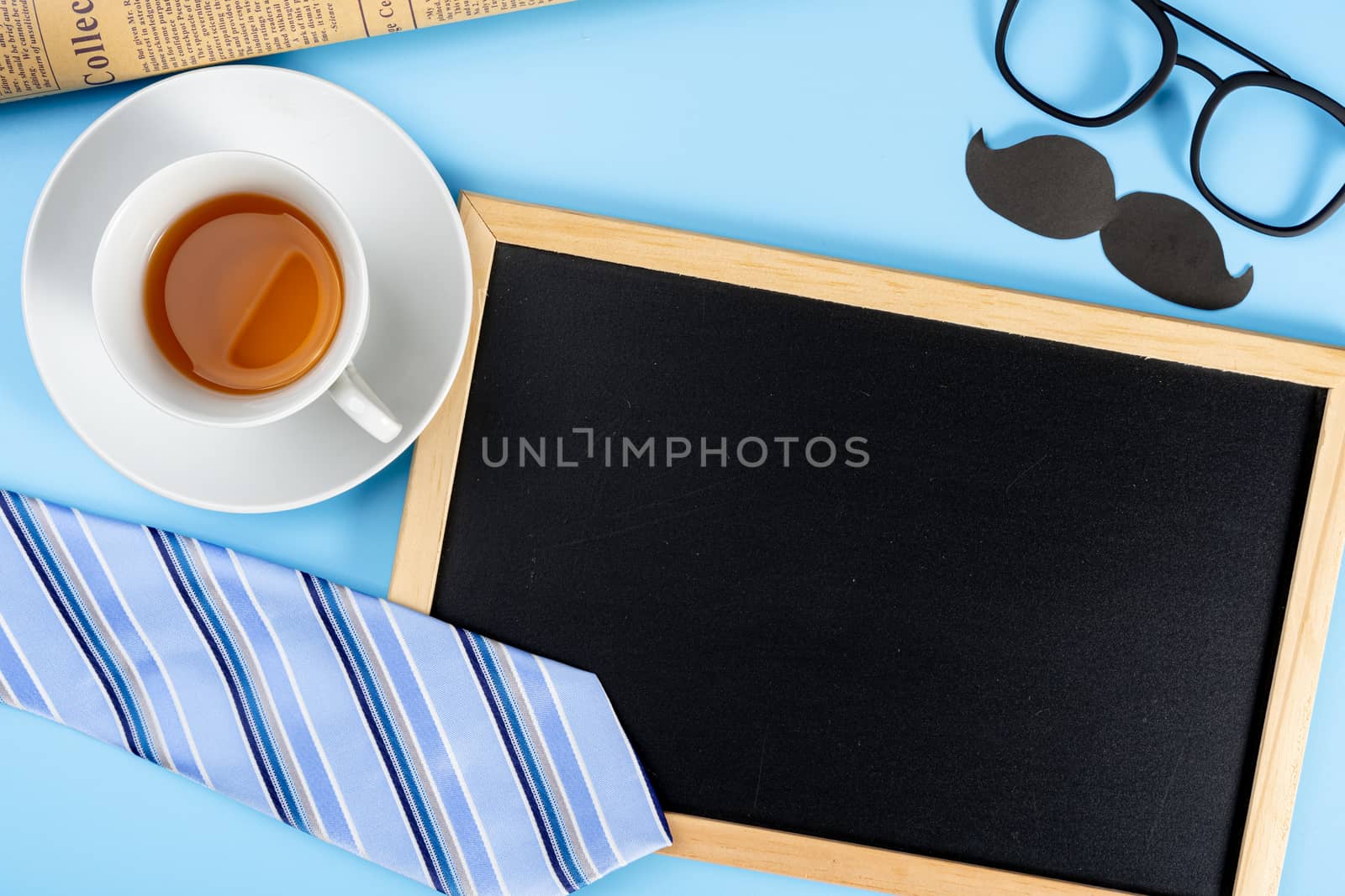 Happy Father Day background concept with blue necktie glasses, newspaper, black mustache, cup of tea and blackboard on blue background with copy space for text.