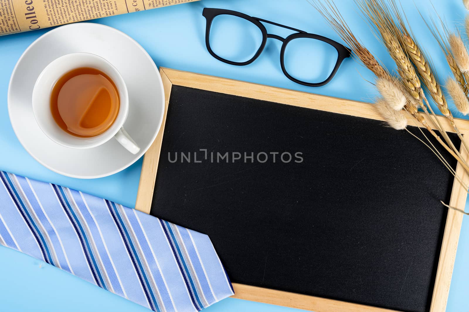 Happy Father Day background concept with blue necktie glasses, newspaper, dry grass flower, cup of tea and blackboard on blue background with copy space for text.