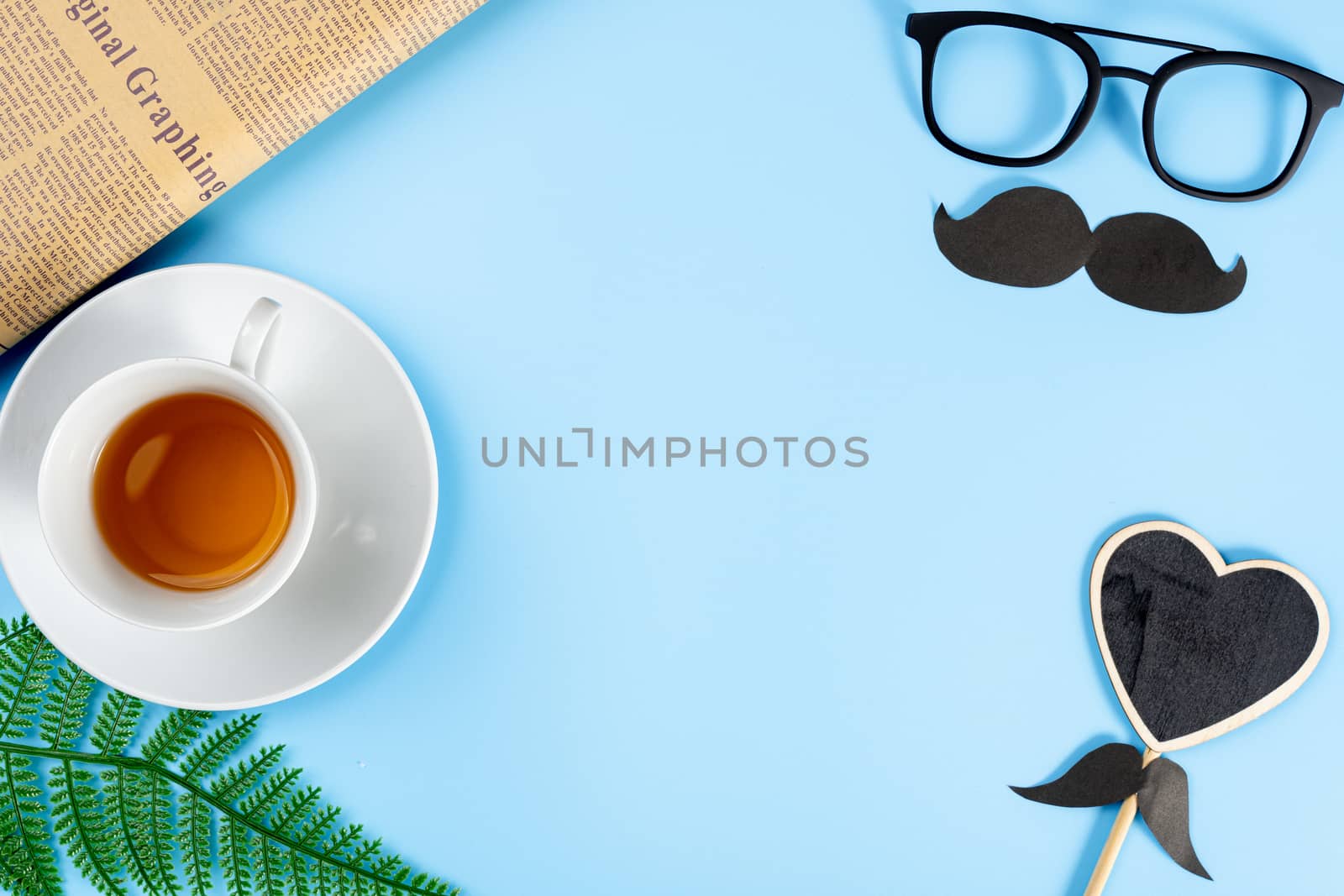 Happy Father Day background concept with glasses, black mustache, heart shape, newspaper, leaf and cup of tea on blue background with copy space for text.