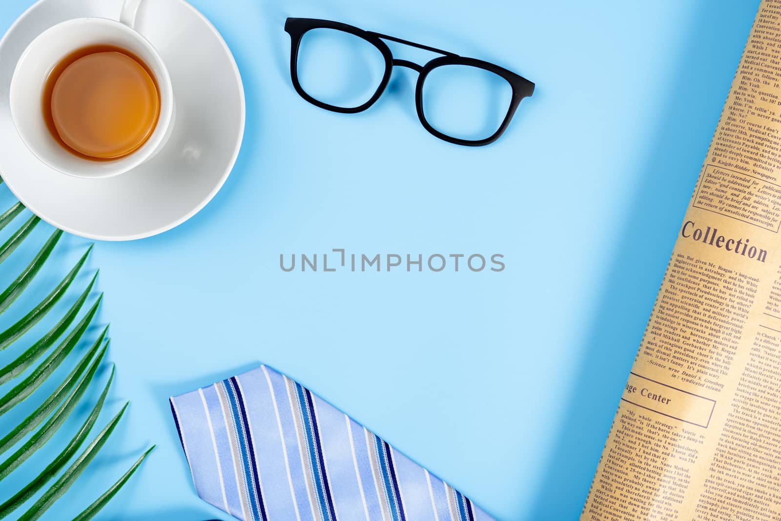 Happy Father Day background concept with blue necktie, glasses, newspaper, leaf and cup of tea on blue background with copy space for text.