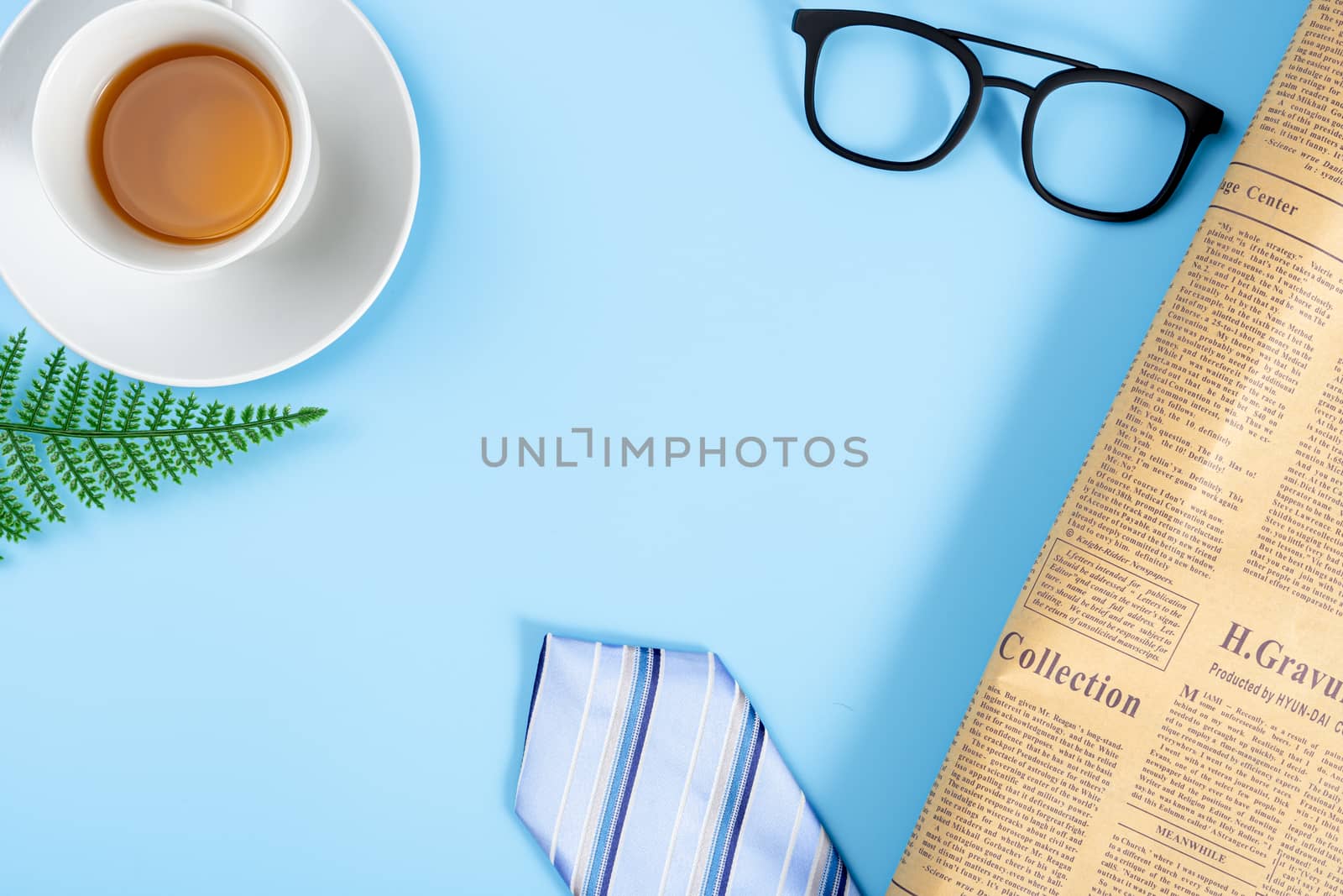 Happy Father Day background concept with blue necktie, glasses, newspaper, leaf and cup of tea on blue background with copy space for text.