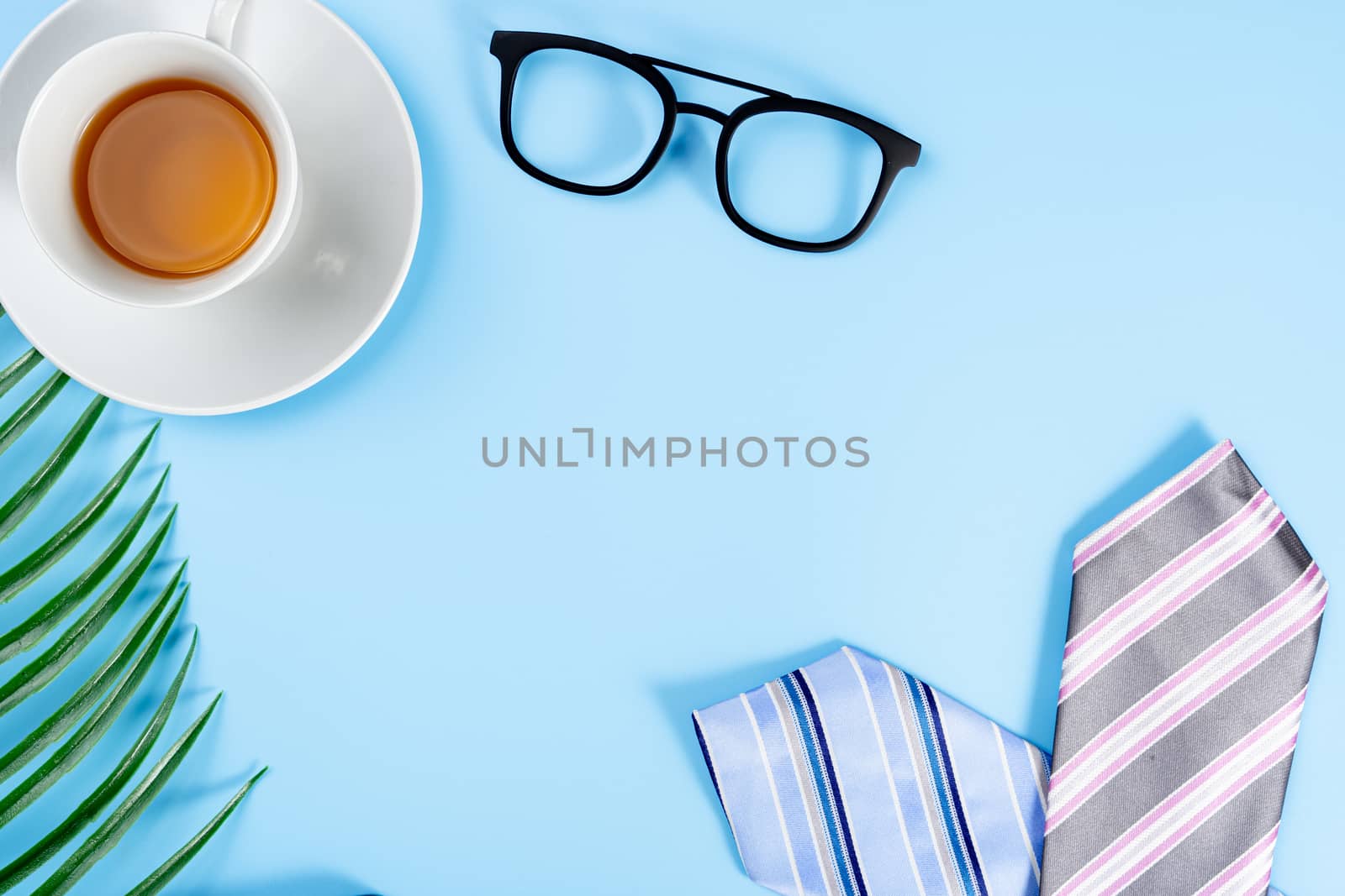 Happy Father Day background concept with blue and pink necktie, glasses, newspaper, leaf and cup of tea on blue background with copy space for text.