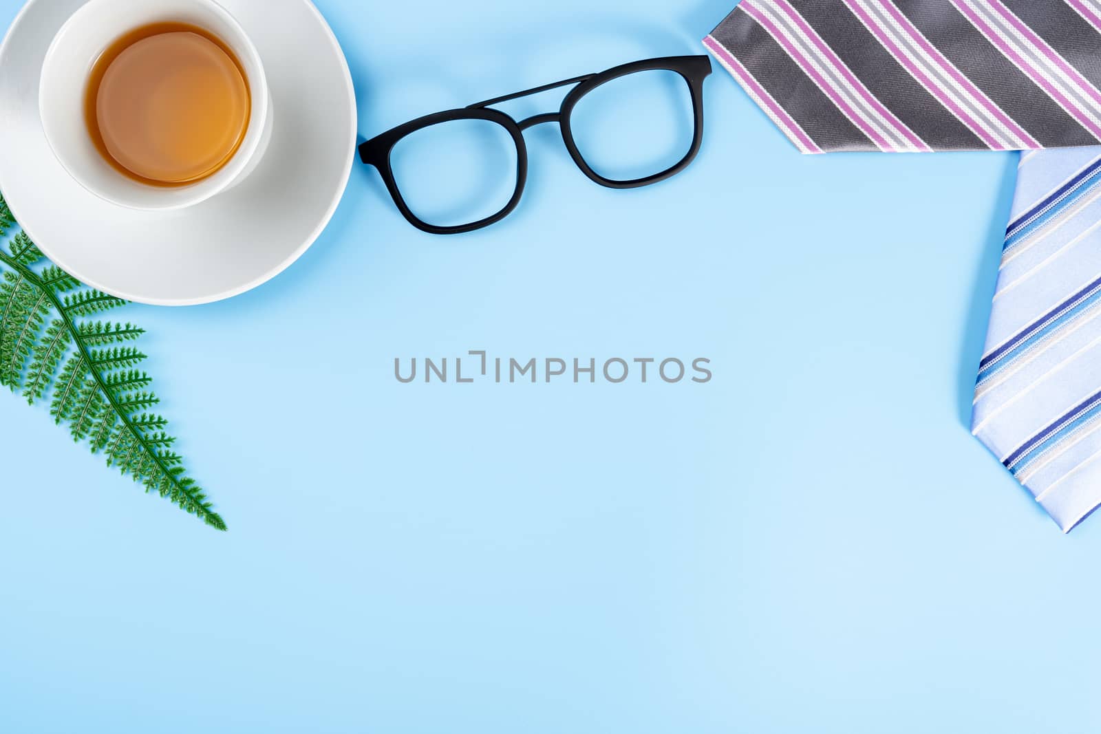 Happy Father Day background concept with pink necktie, glasses, newspaper, leaf and cup of tea on blue background with copy space for text.