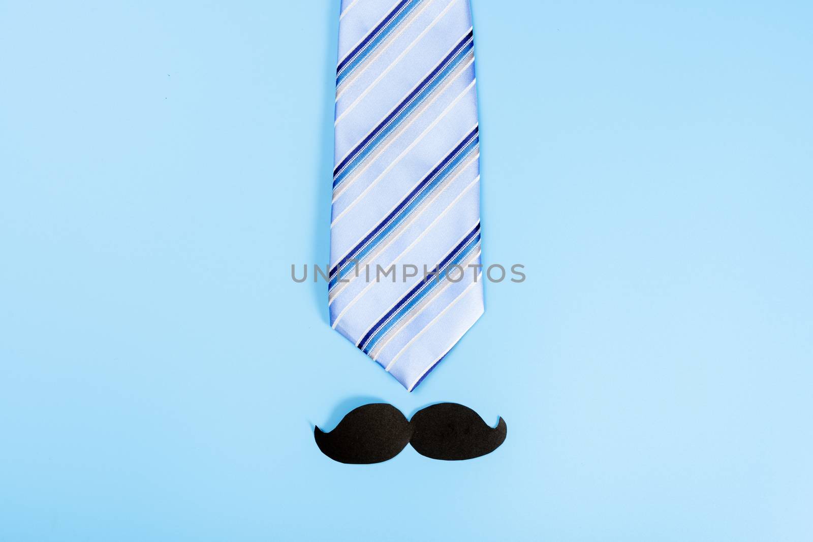 Happy Father Day background concept with blue necktie and black mustache on blue background with copy space for text.