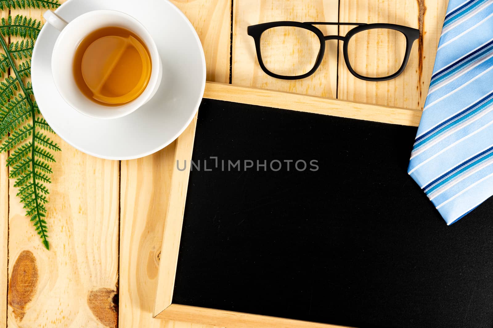 Happy Father Day background concept with blue necktie, glasses, cup of tea and blackboard on wooden background with copy space for text.
