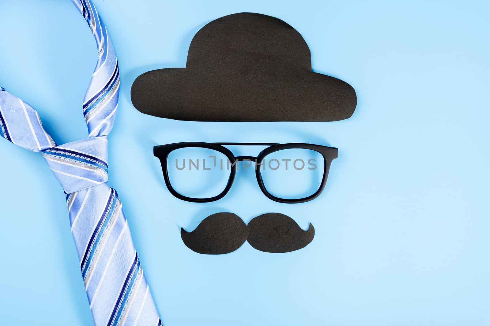 Happy Father Day background concept with blue necktie, glasses, black hat and black mustache on blue background with copy space for text.