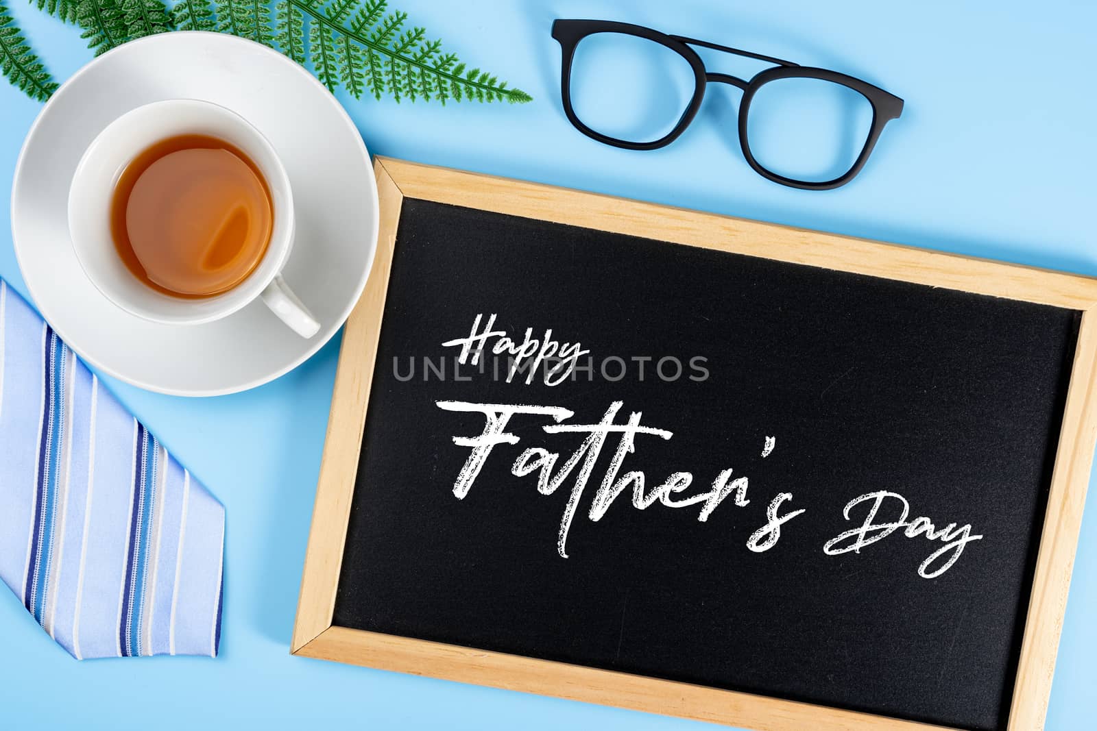 Happy Father Day background concept with blue necktie glasses, leaf, cup of tea and blackboard on blue background with copy space for text.