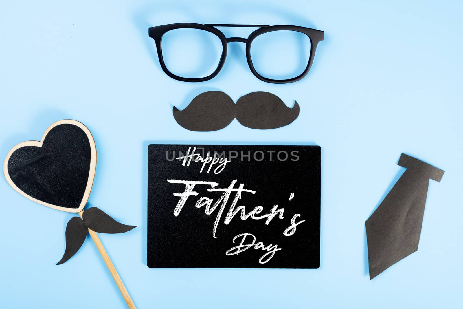 Happy Father Day background concept with glasses, blackboard, black heart shape, tie and black mustache on blue background with copy space for text.
