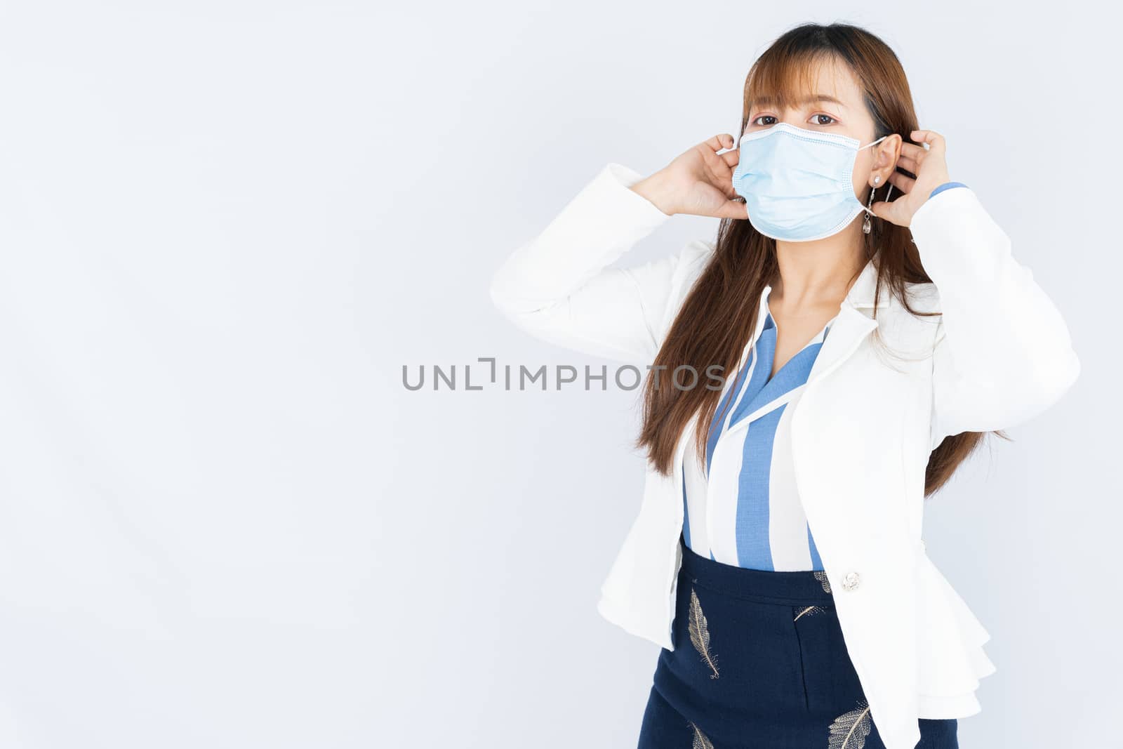 Smiling Asian business woman wearing a medical face mask and looking at the camera the over grey background. Back to the normal concept.