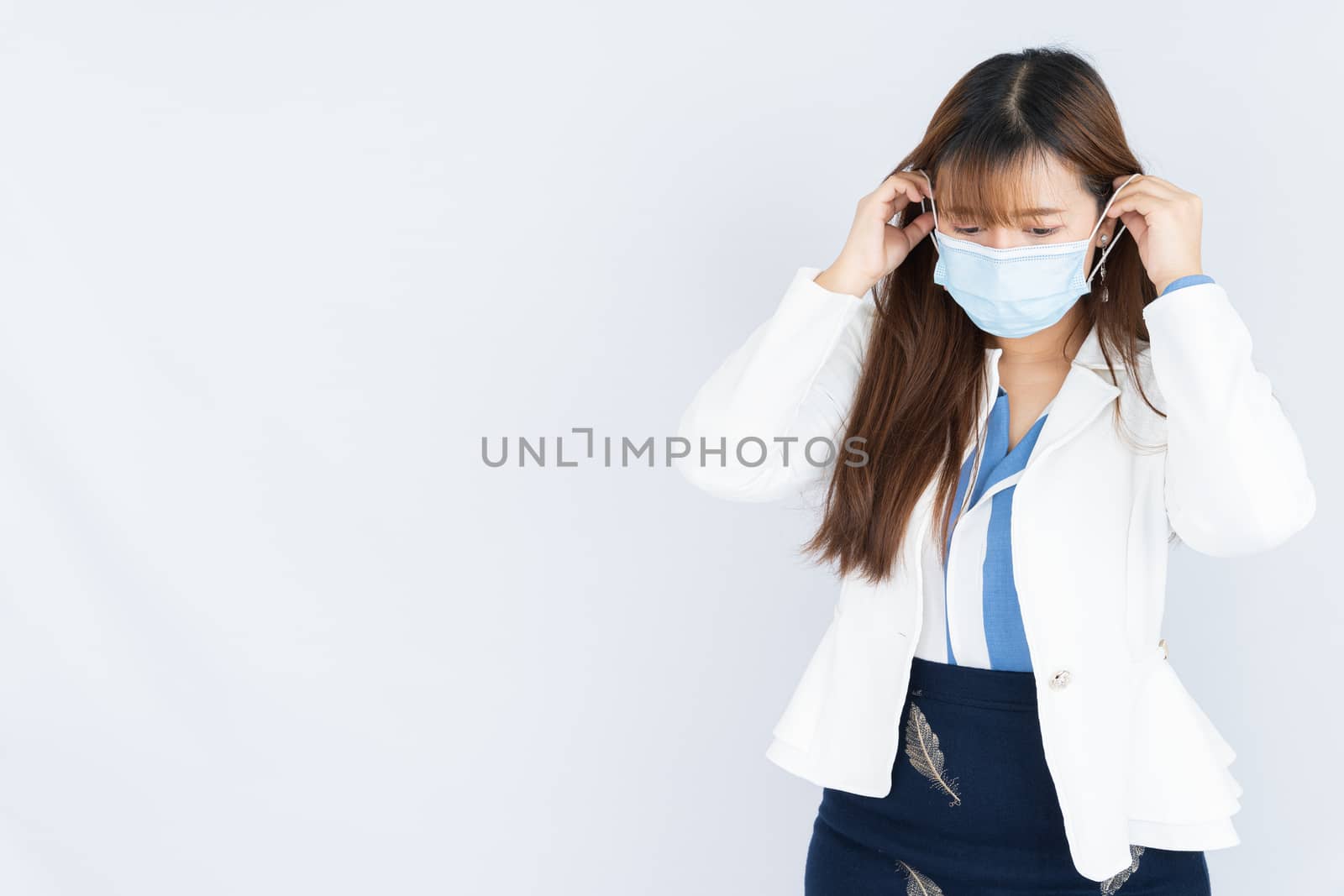 Smiling Asian business woman wearing a medical face mask and looking at the camera the over grey background. Back to the normal concept. by mikesaran
