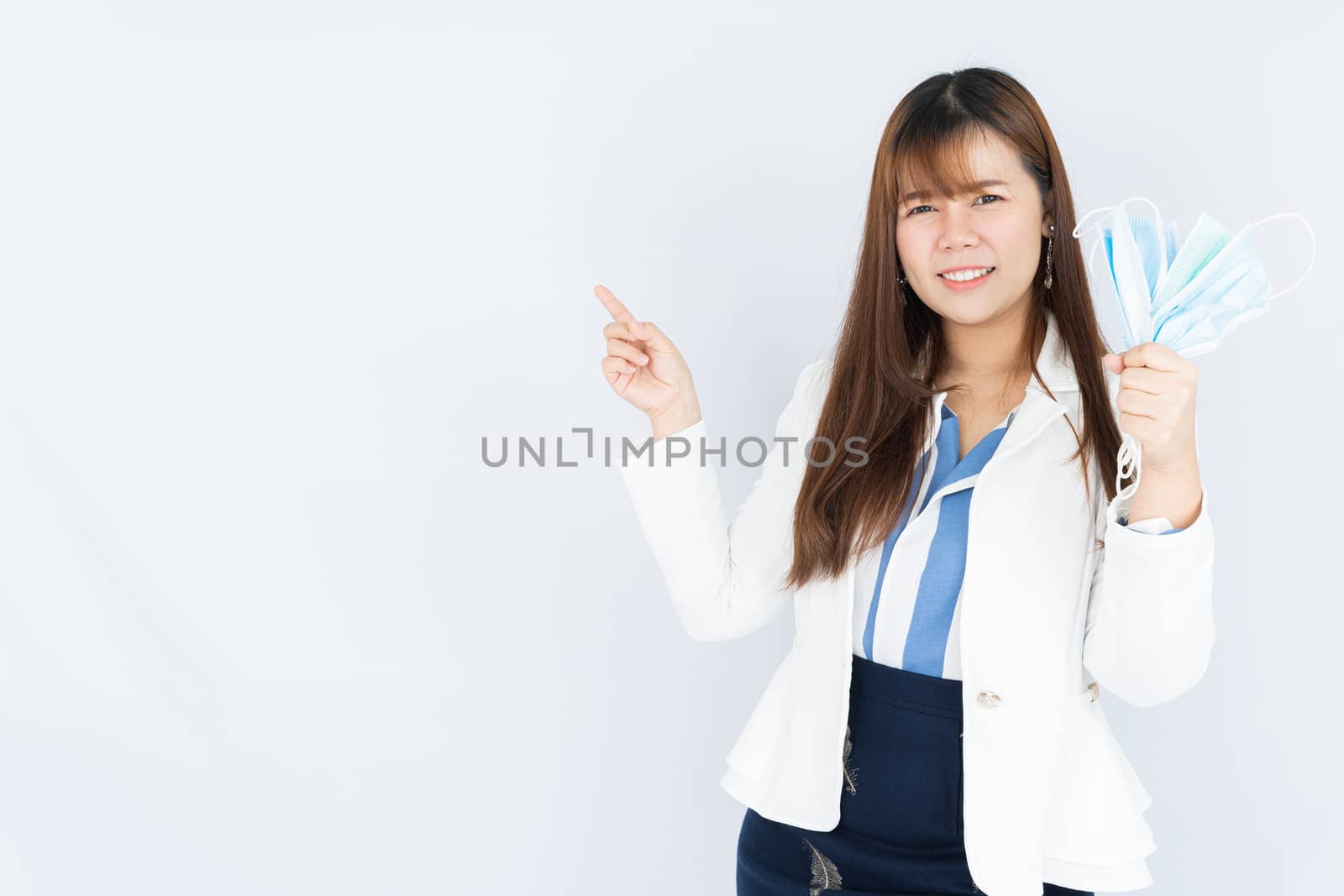 Smiling Asian business woman holding the showing face mask and pointing finger to side blank space over grey background. Back to the normal concept.