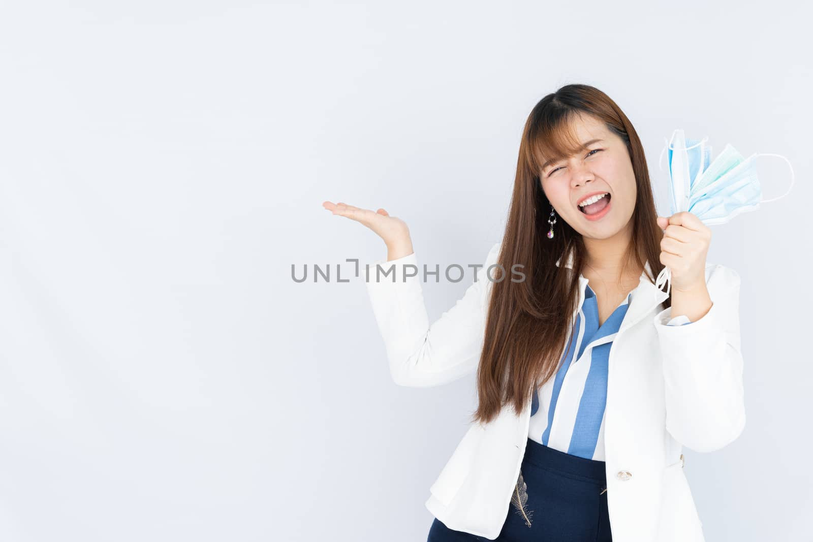 Smiling Asian business woman holding the showing face mask and pointing finger to side blank space over grey background. Back to the normal concept.