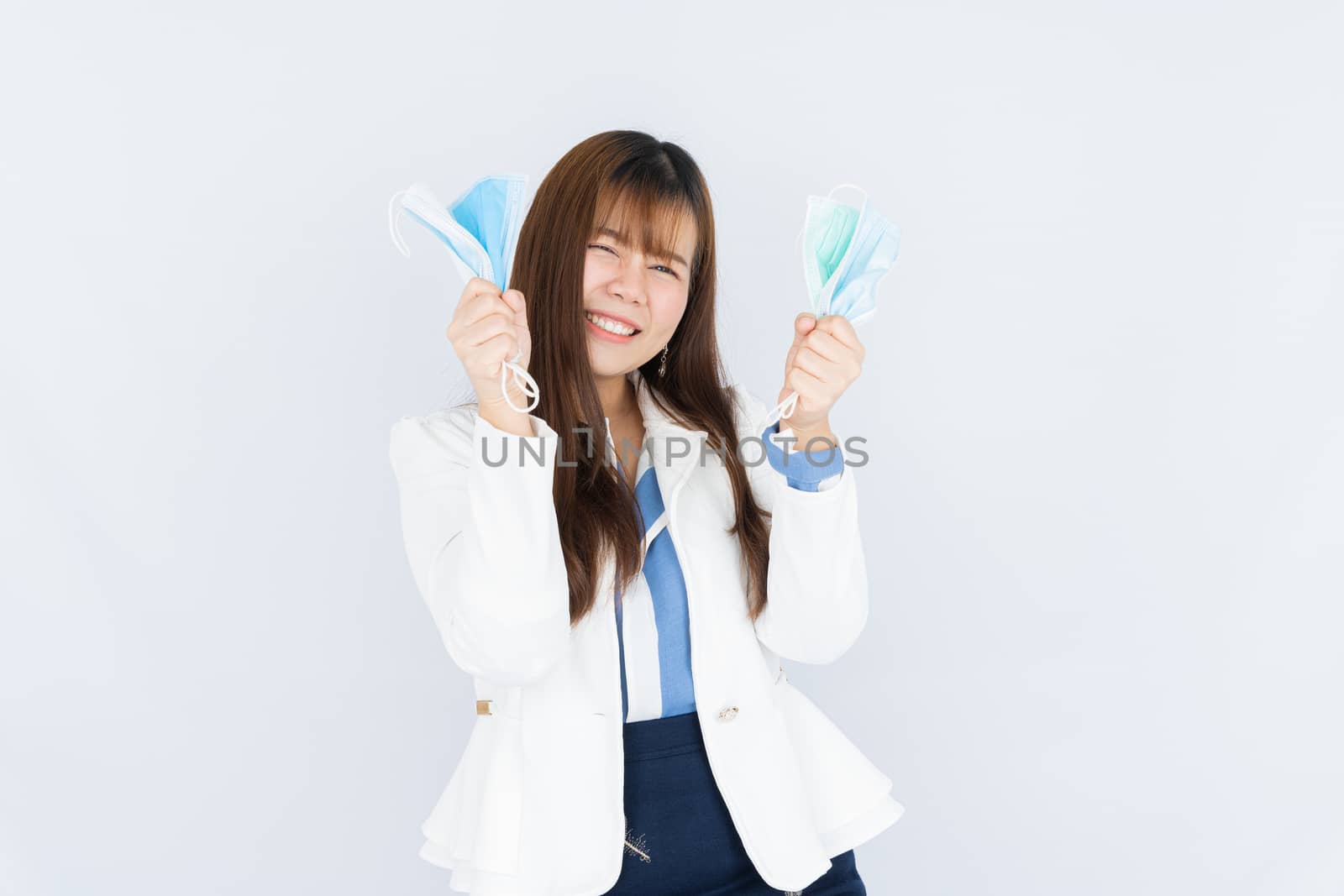 Smiling Asian business woman shows hand grasping mask over grey background. Back to the normal concept.