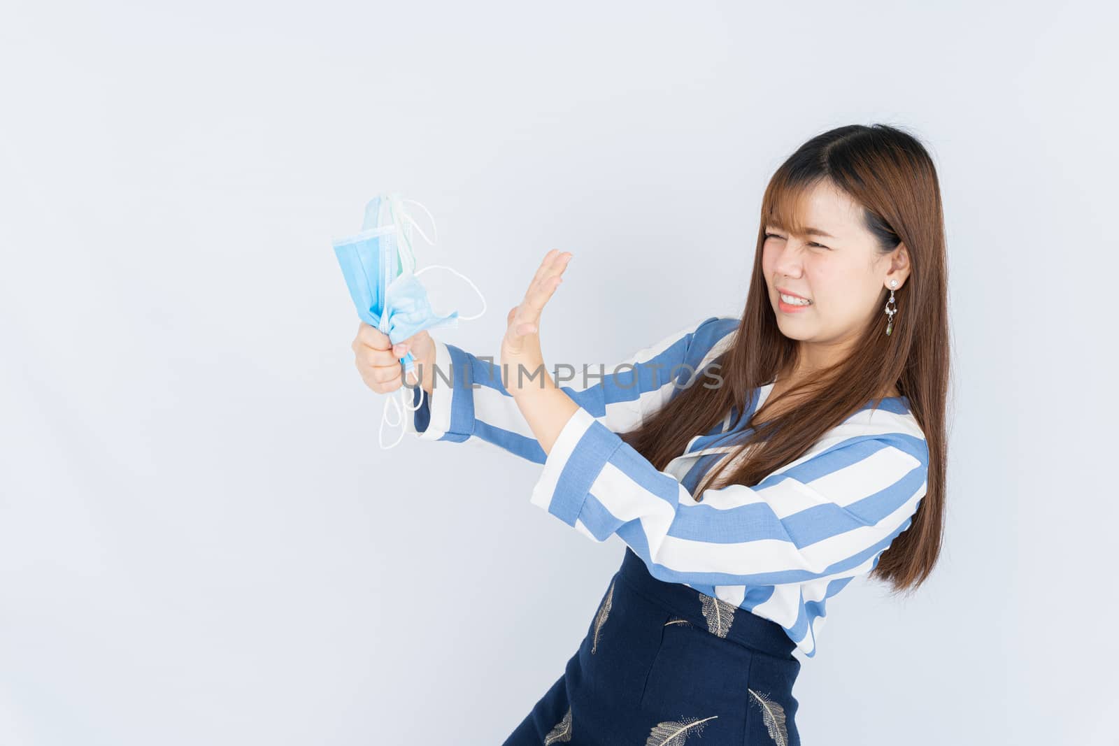Smiling Asian business woman shows hand grasping mask and goodbye hand sign to the mask over grey background. Back to the normal concept.