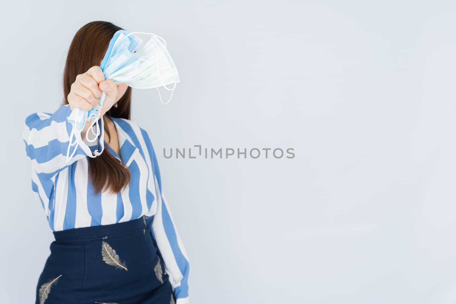 Business woman shows hand grasping mask over grey background. Back to the normal concept. by mikesaran