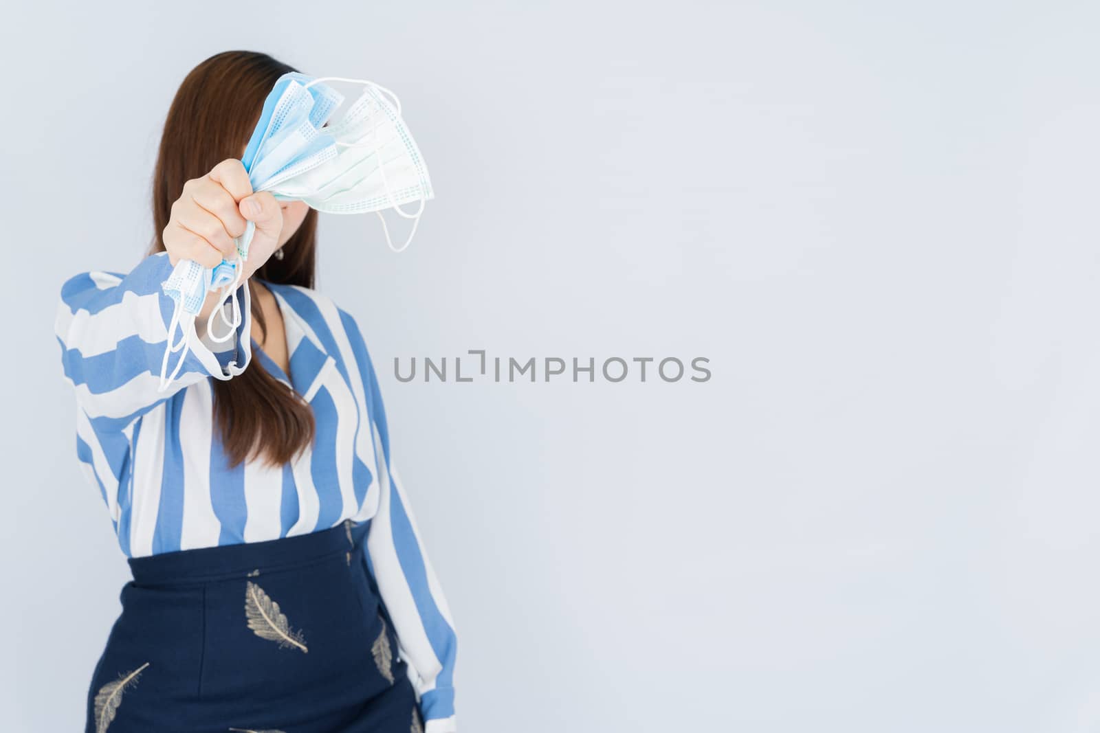 Business woman shows hand grasping mask over grey background. Back to the normal concept.